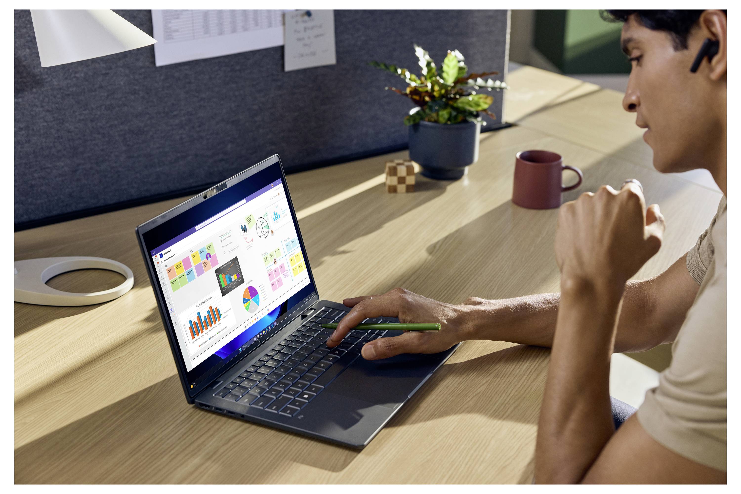 Person, die am Schreibtisch in einem modernen Büro bunte Diagramme und Grafiken auf einem Laptop analysiert und dabei einen Stift in der Hand hält.