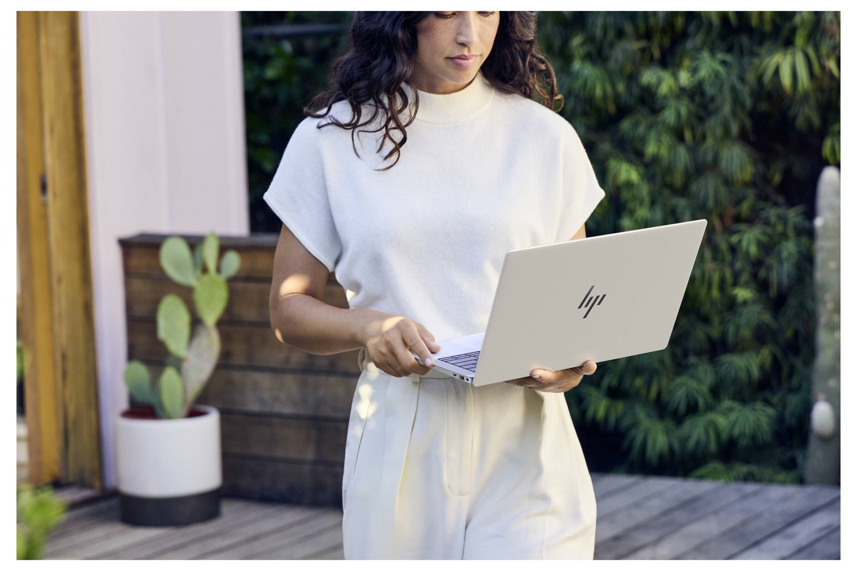 Frau, die draußen einen Laptop benutzt, konzentriert auf den Bildschirm in einer Terrassen- oder Gartenumgebung.
