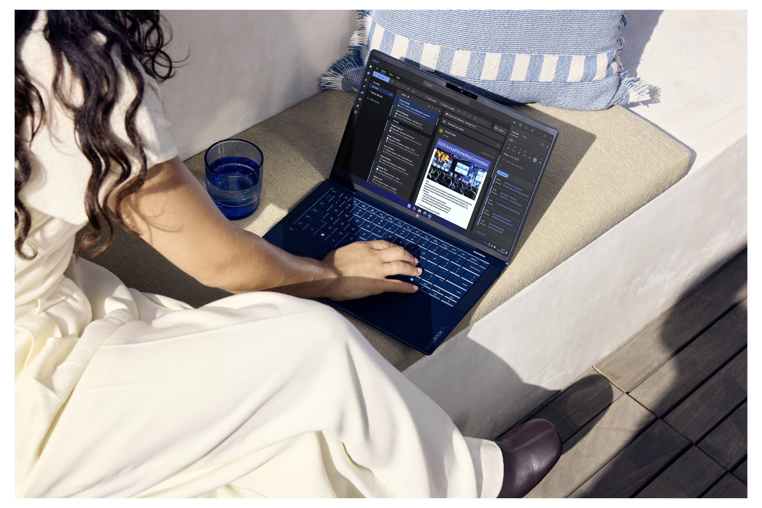 Frau, die einen Laptop auf einem Sofa im Freien benutzt, arbeitet an einer Website- oder App-Oberfläche neben einem blauen Glas und einem gestreiften Kissen.