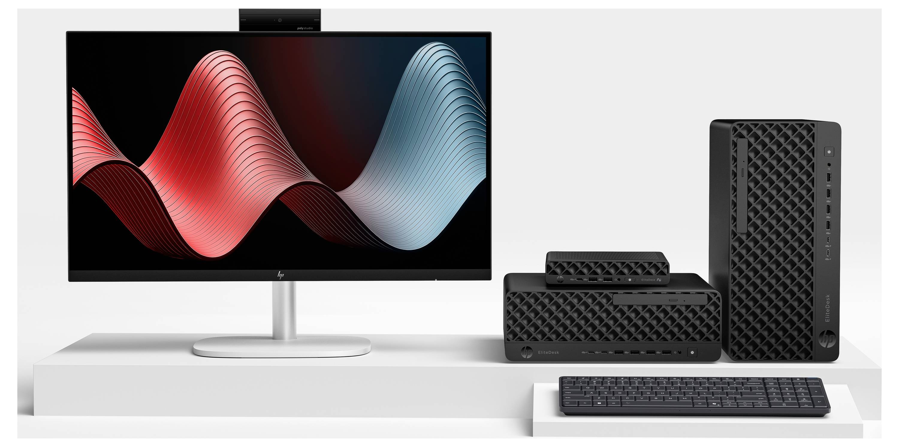 Desktop-Computer-Setup mit Breitbildmonitor, der abstrakte rote und blaue Wellengrafiken anzeigt, sowie kleinem PC-Turm, Lautsprecher und Tastatur auf einem weißen Schreibtisch.