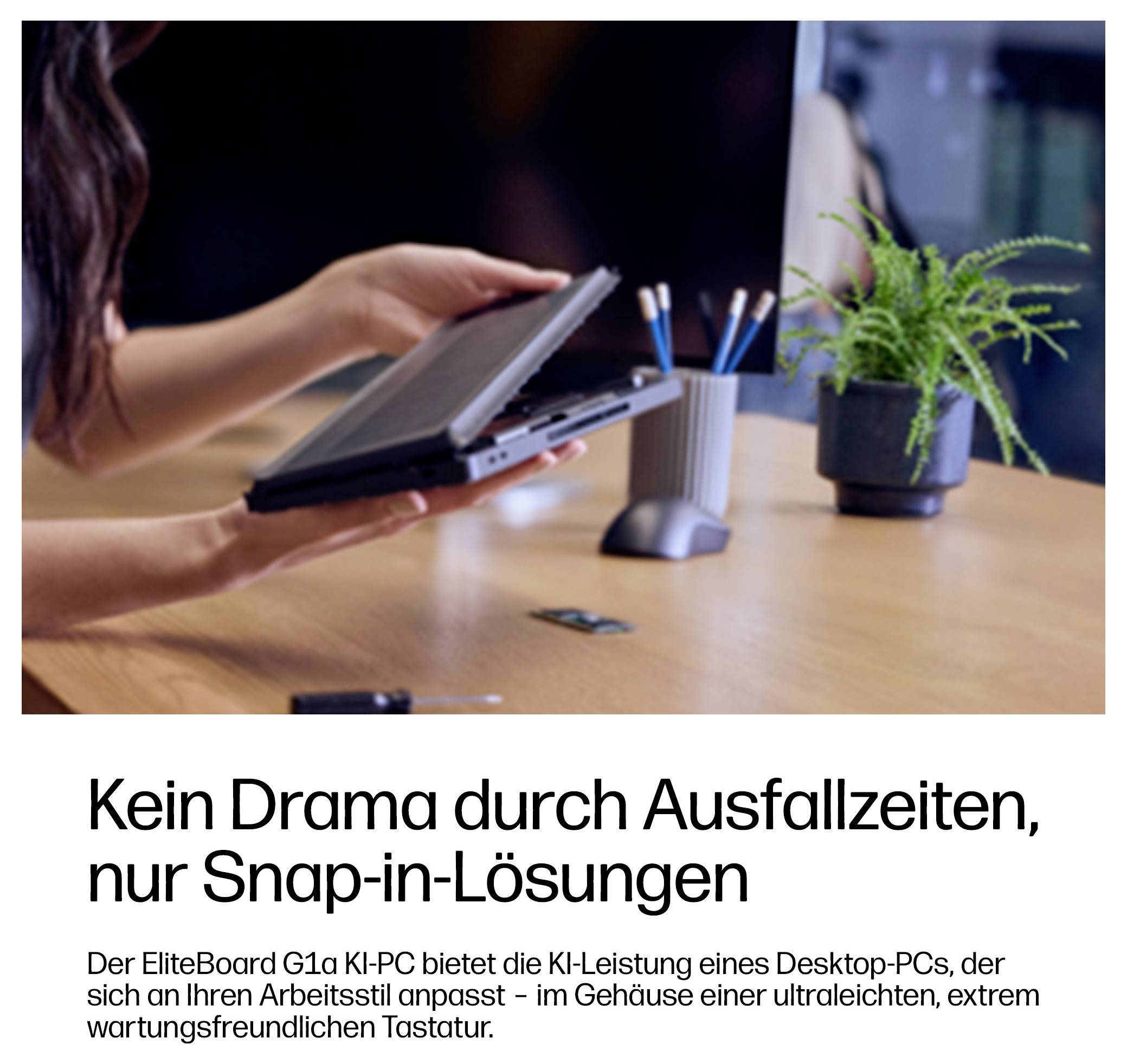 Hände halten ein kompaktes, laptopähnliches Gerät neben einer Schreibtischpflanze, mit deutschem Anzeigentext darunter, der 