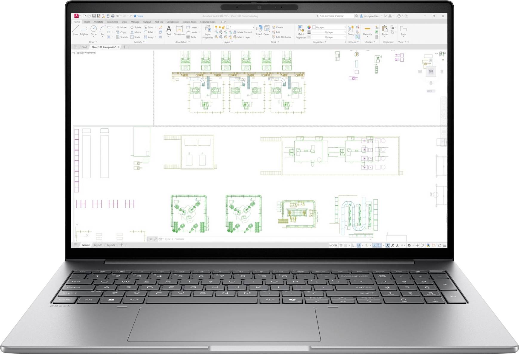 Laptop mit einer CAD-Grundrisszeichnung mit mehreren Raumlayouts und technischen Annotationen auf einem weißen Arbeitsplatz.