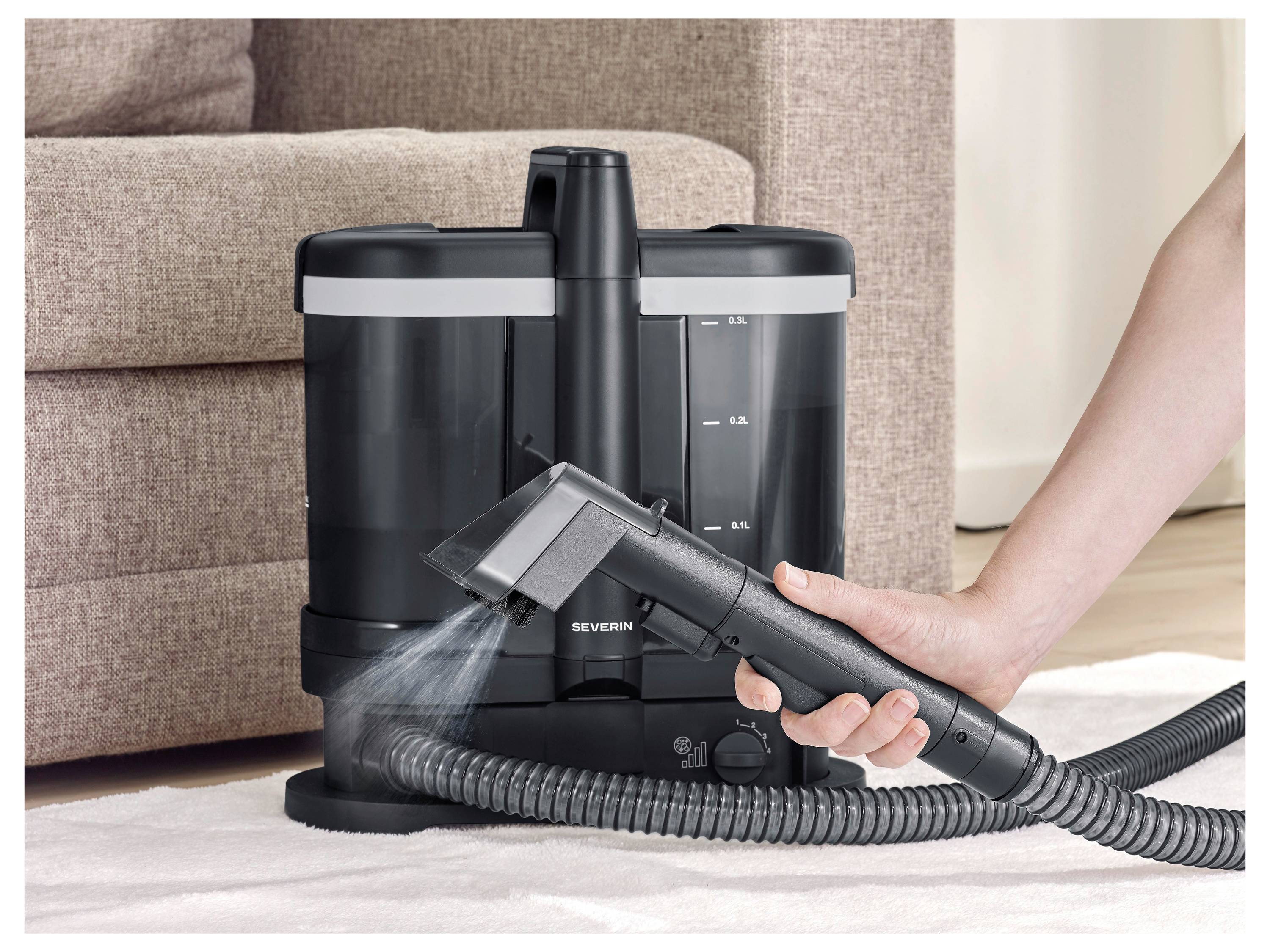 Eine Hand verwendet eine Dampfreiniger-Aufsatz, um Dampf von einer schwarzen Bodenreinigungsmaschine auf einen Teppich neben einem Sofa zu sprühen.