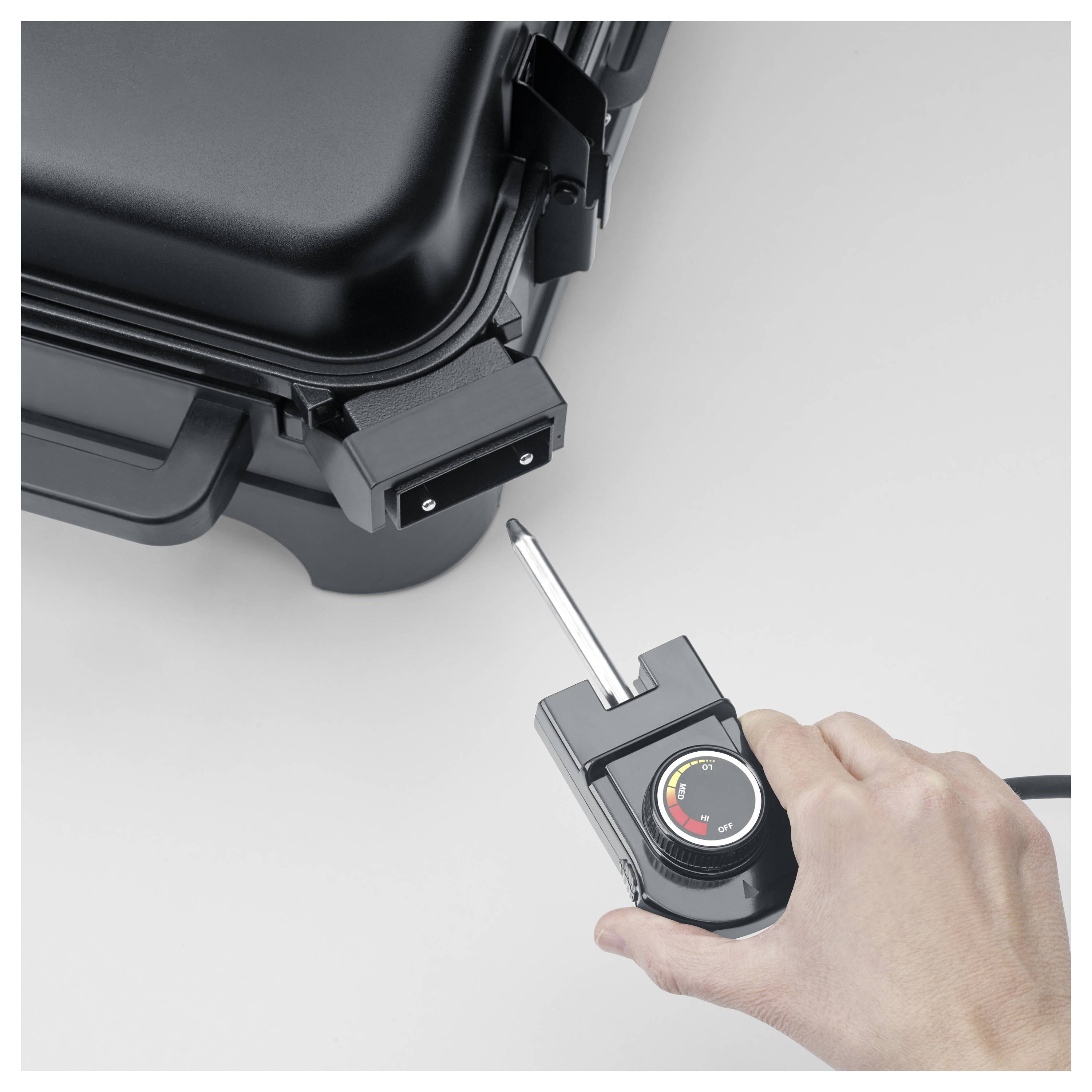 Hand, die eine Sonde in der Nähe eines Steckers eines schwarzen Geräts hält, was auf eine Verbindung oder ein Temperaturregelungssetup hindeutet.