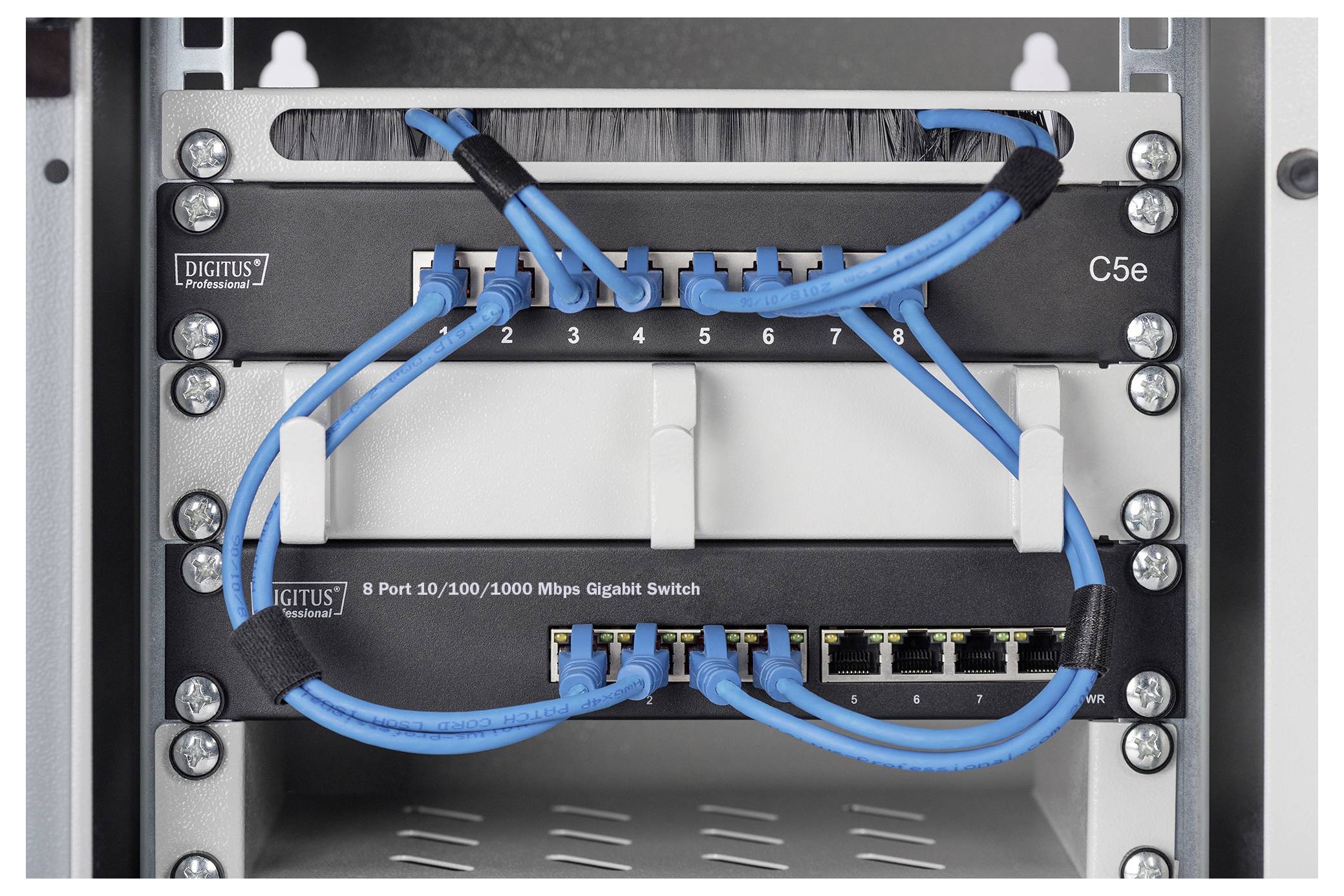 Nahaufnahme von Netzwerkausrüstung in einem Rack: zwei DIGITUS-Switches mit blauen Ethernet-Kabeln, die mit nummerierten Anschlüssen verbunden sind.