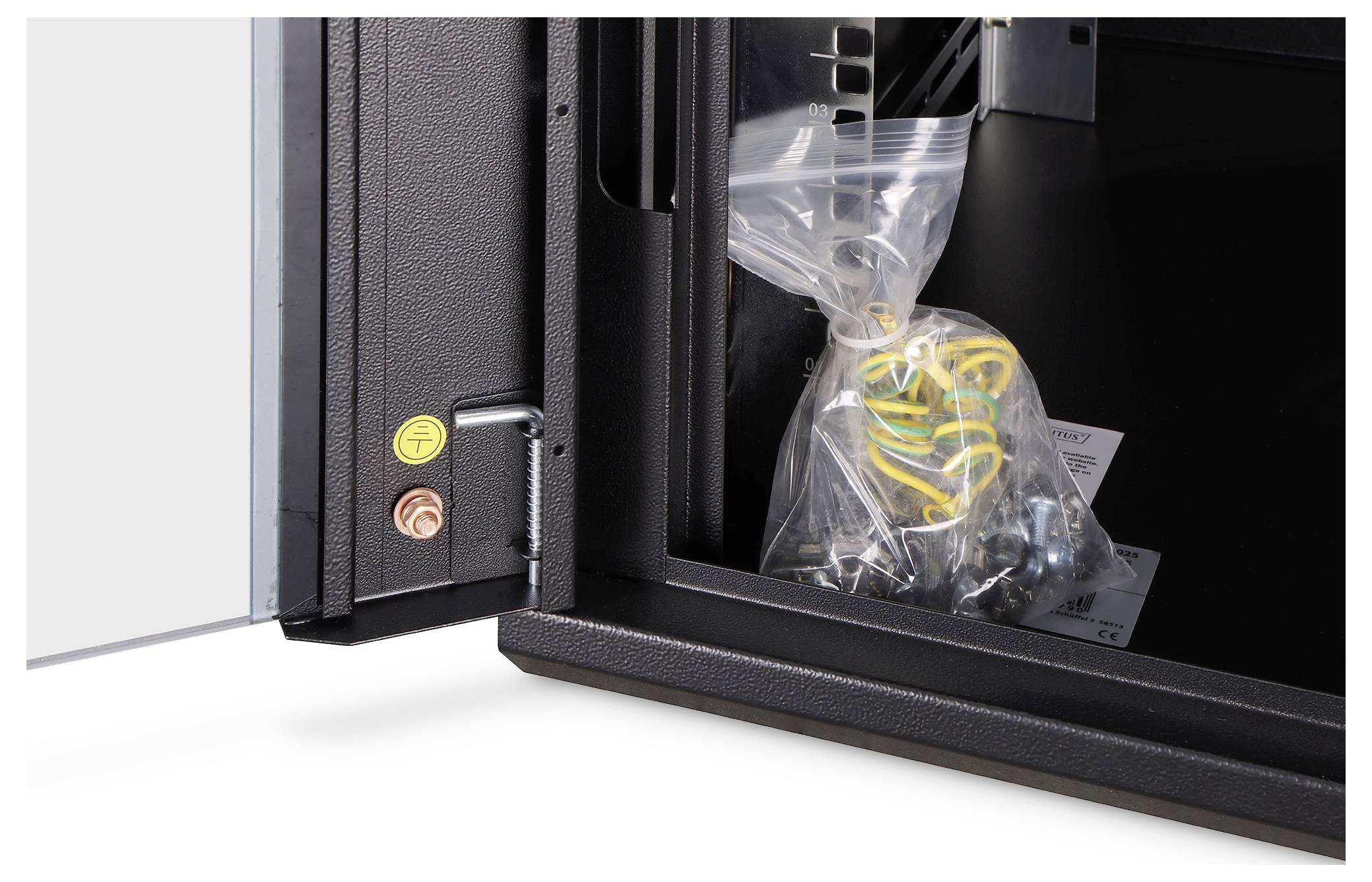 Offener schwarzer Schrank oder Druckerbereich mit einer klaren Tasche mit Kabeln und Ersatzteilen im Inneren, sowie gelben und roten Steuertasten an der Tür.
