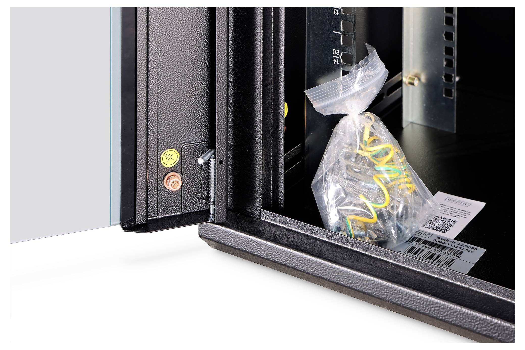 Offener Schrank mit einer Plastiktüte voller Kabel und Etiketten im Inneren; auf der linken Seite sind zwei farbige Tasten sichtbar.