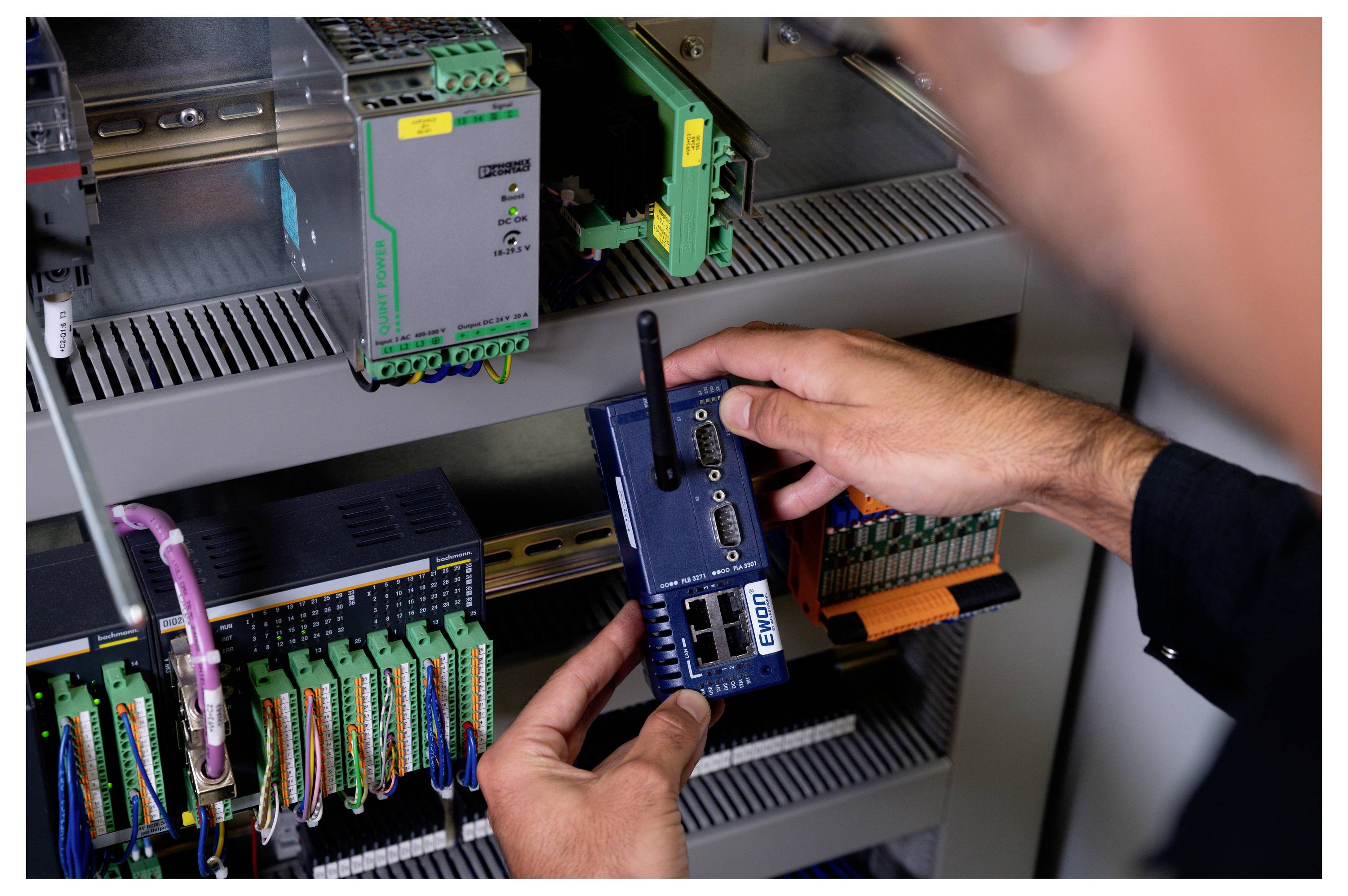 Ein Techniker installiert ein blaues Ethernet-/Netzwerkgerät in einen Industriesteuerungsschrank mit Verdrahtung und montierten Modulen.