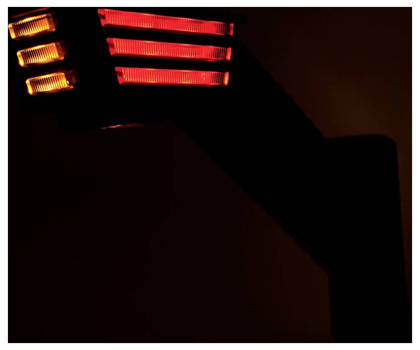Nahaufnahme einer dunklen Lampe oder eines Heizers mit leuchtenden rot und orange gefärbten Heizelementen vor schwarzem Hintergrund.