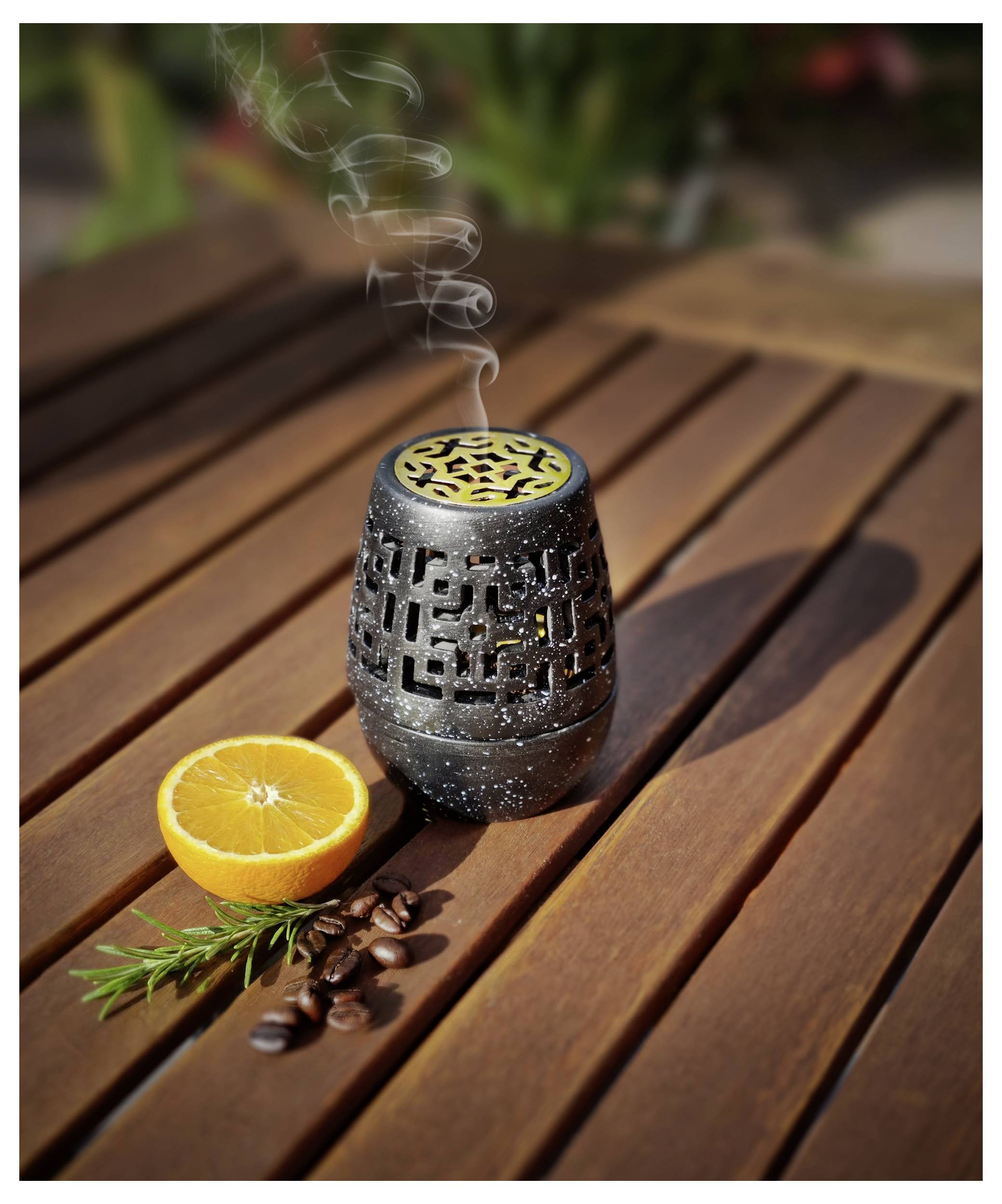 Ein beleuchteter dekorativer Aromadiffuser auf einem Holztisch gibt Dampf ab und steht neben einer halbierten Orange, einem Rosmarinzweig und Kaffeebohnen.
