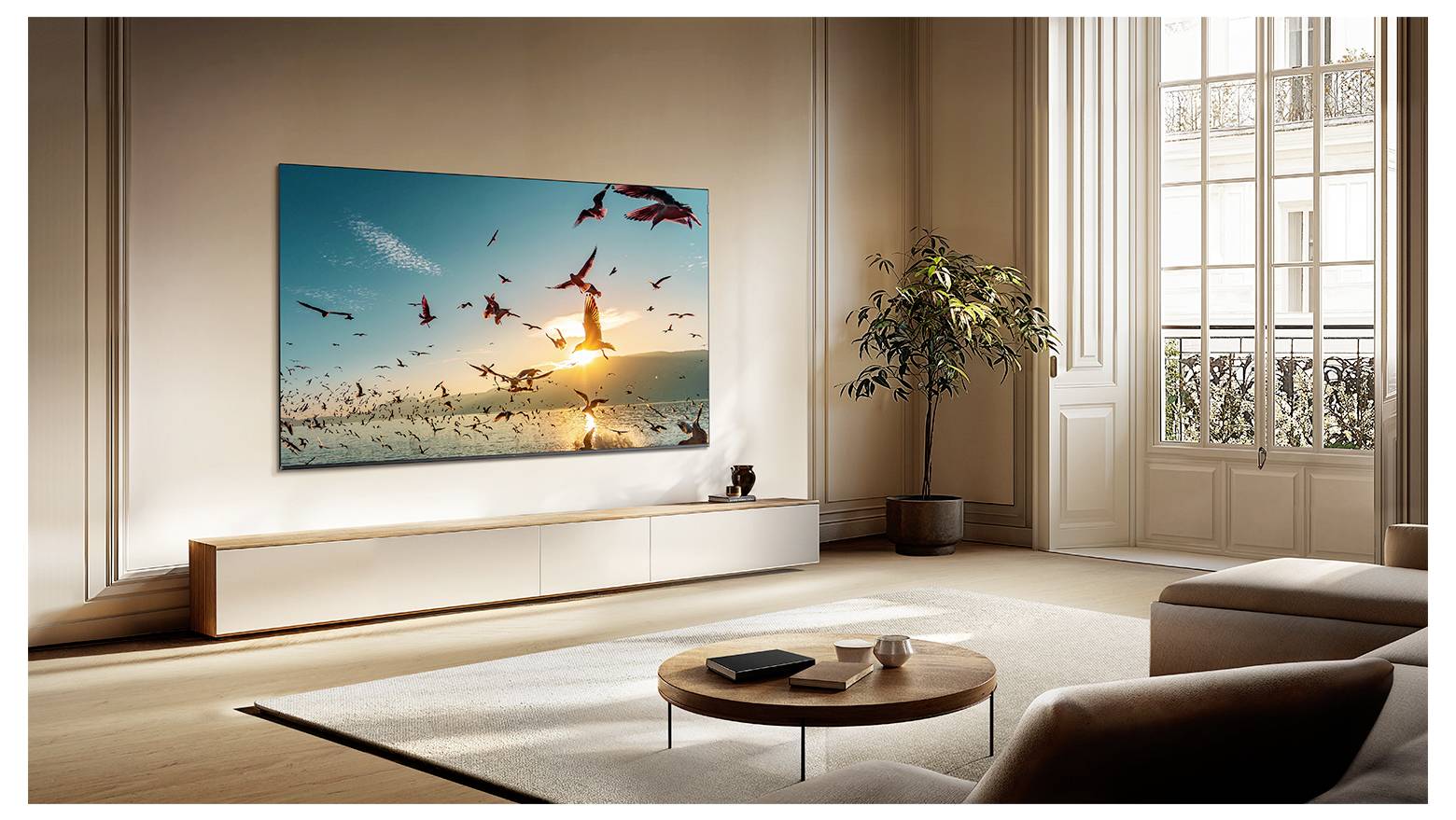 Modernes Wohnzimmer mit großem Wandkunstwerk von Vögeln, die über einen Sonnenuntergangsstrand fliegen, einer niedrigen Konsole, Couchtisch, Sofa, Pflanze und großen Fenstern.