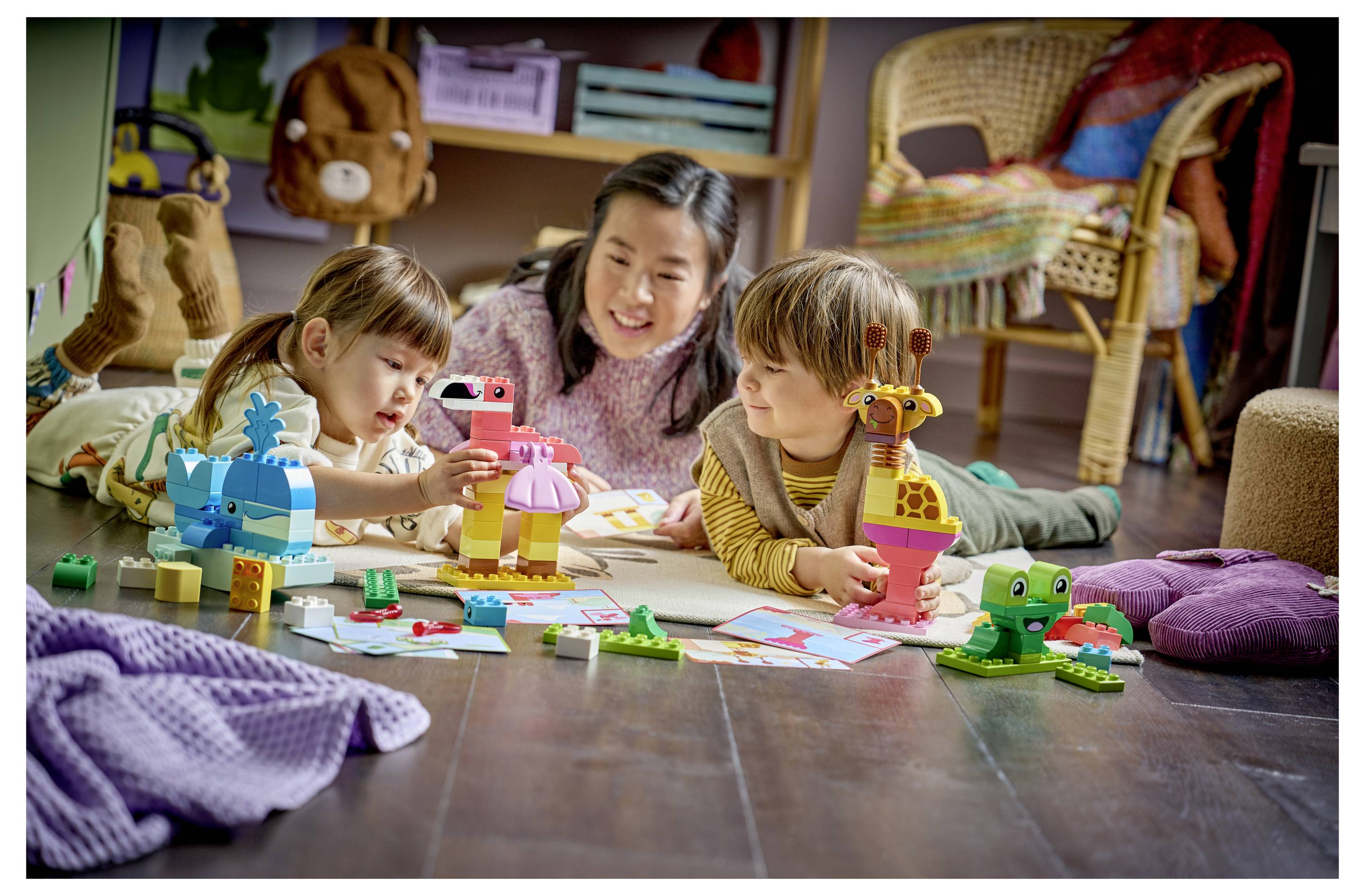 Drei Kinder spielen mit bunten Bausteinen und Spielzeugtieren auf dem Boden in einem gemütlichen Wohnzimmer.