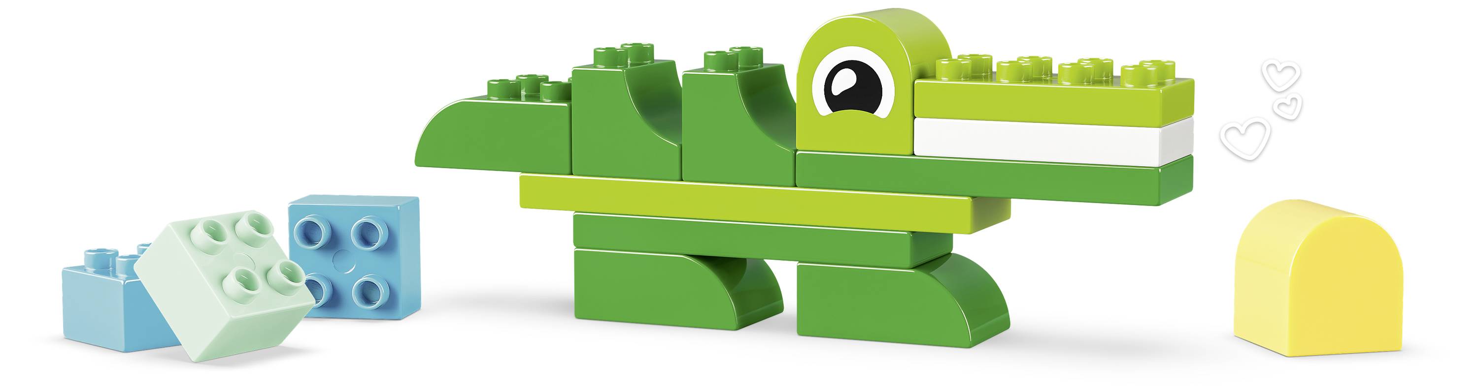 Grünes Spielzeugkrokodil aus Bausteinen gebaut, mit zwei losen Bausteinen in der Nähe und einem gelben Baustein auf der rechten Seite.