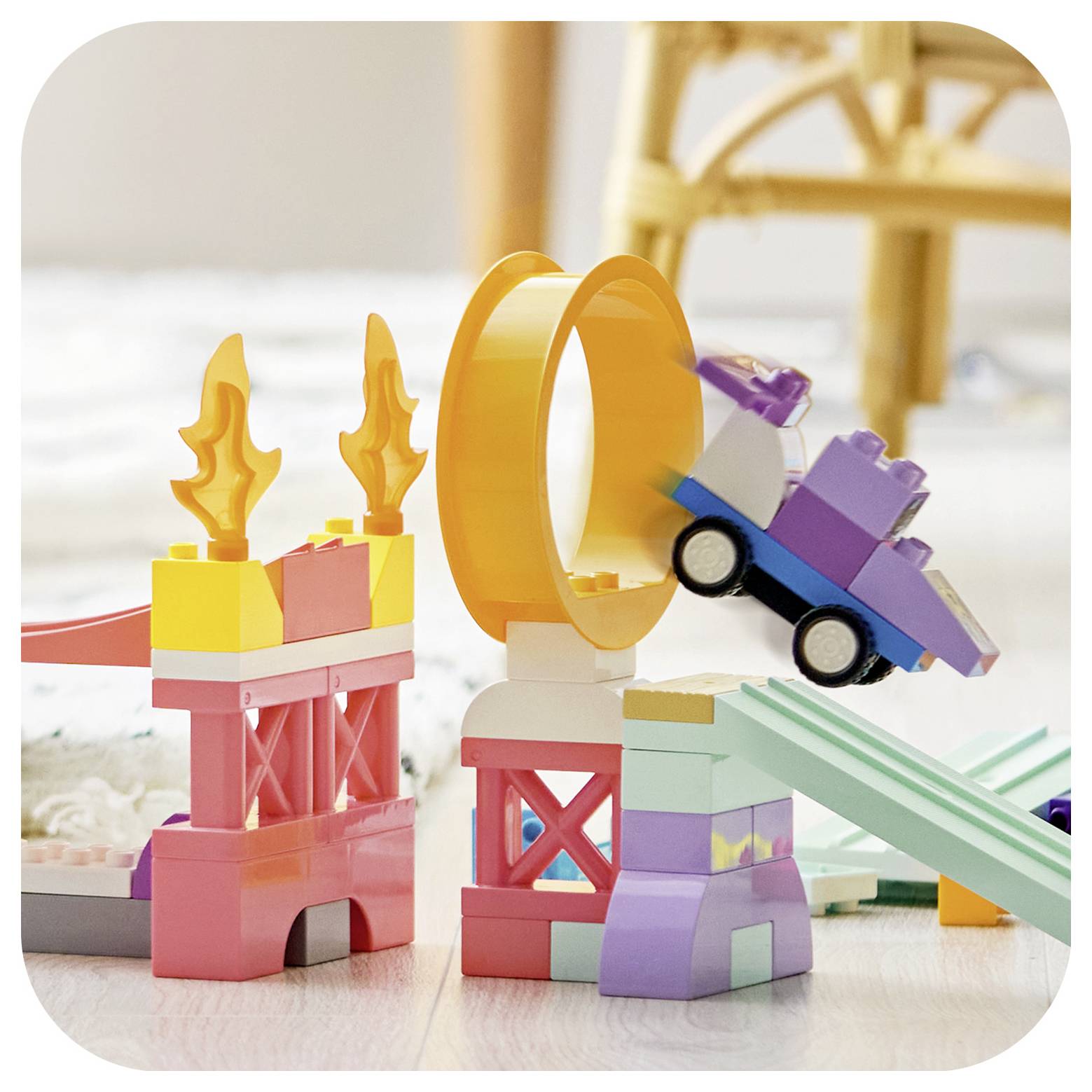 Bunte Spielzeugbausteine bilden eine Feuer-Sprung-Rampe, wobei ein kleines violettes Auto durch einen orangefarbenen Ring springt.