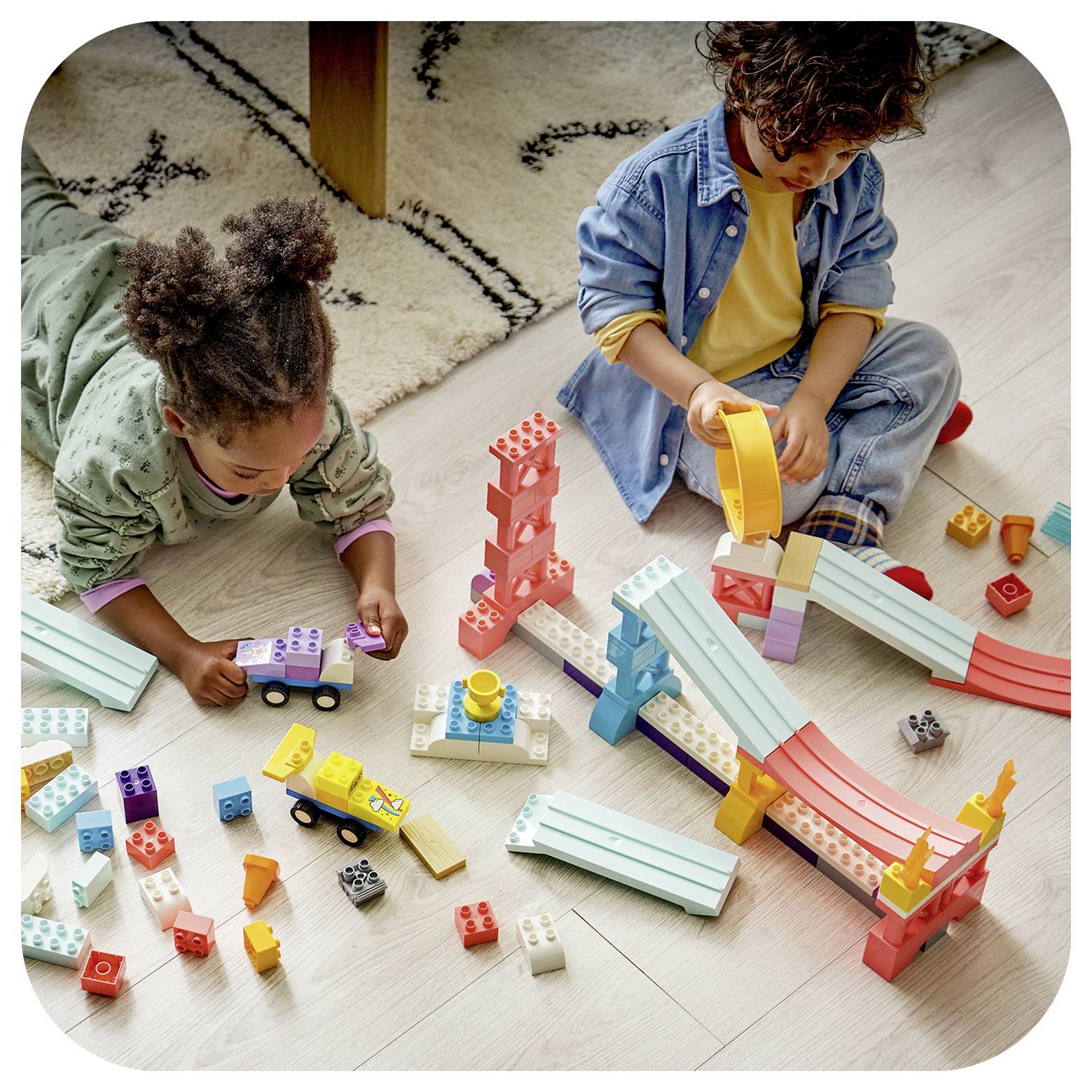 Zwei Kinder spielen mit bunten Bauklötzen und Rampen auf dem Boden und bauen eine Murmelbahn-ähnliche Struktur.