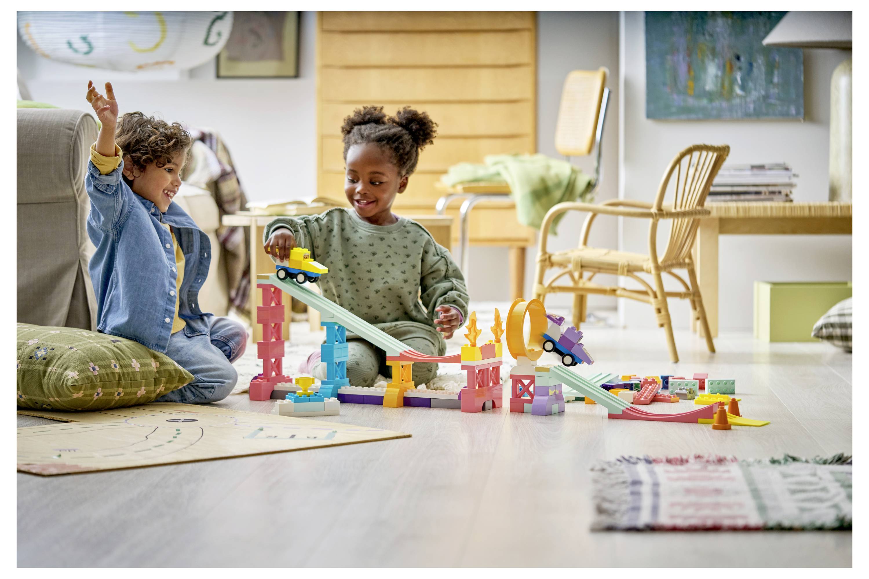 Zwei Kinder spielen mit einer farbenfrohen Spielzeugmurmelbahn in einem hellen Wohnzimmer.