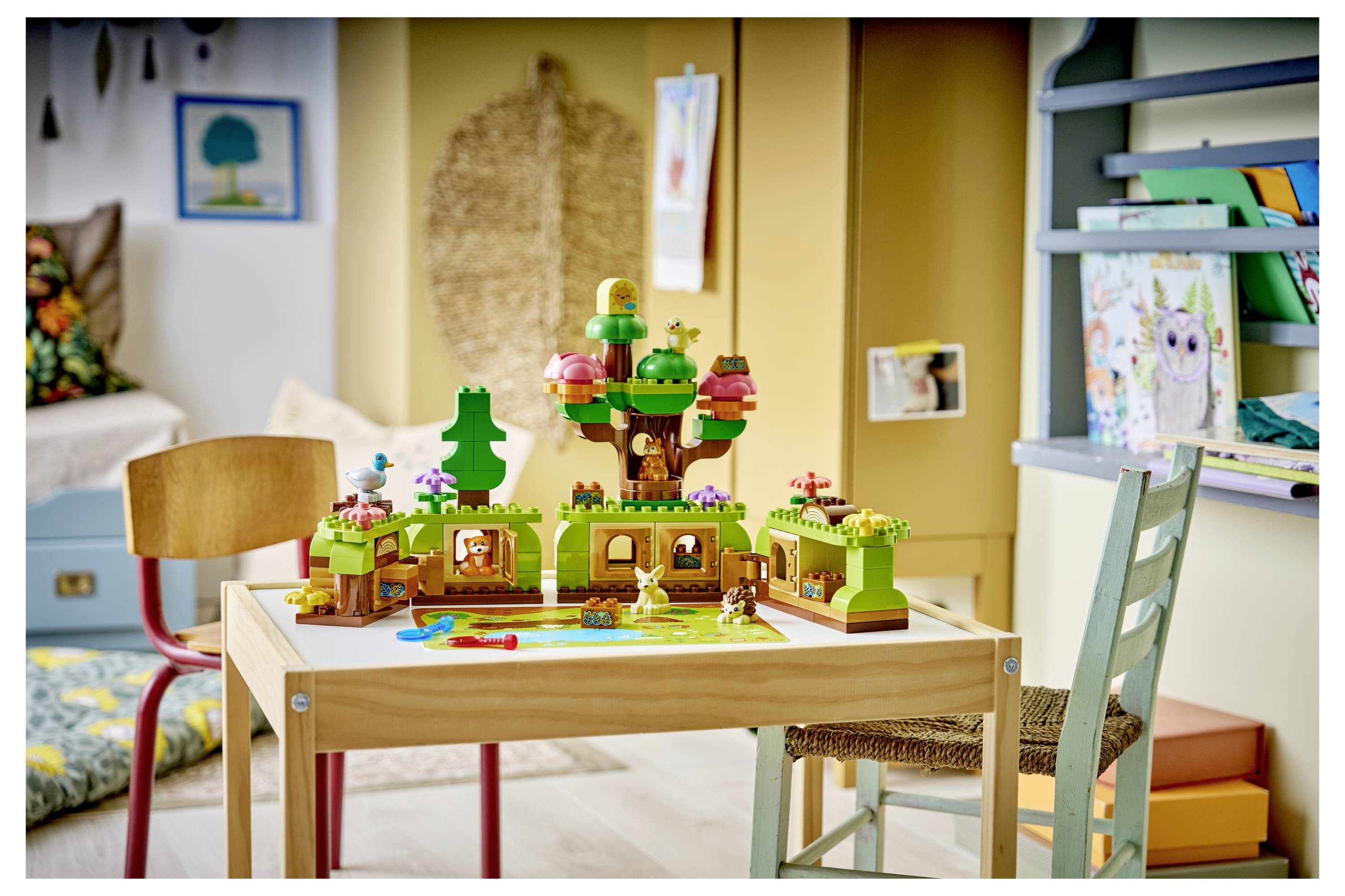 LEGO-ähnliches Baumhaus-Spielset auf einem kleinen Holztisch in einem Kinderzimmer gebaut, mit Stühlen und Regalen rundherum.