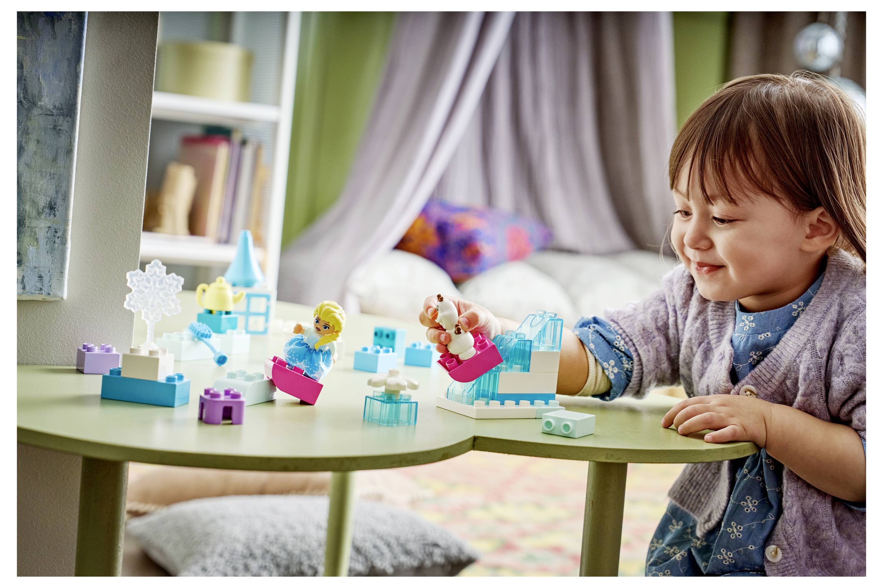 Kleines Kind, das mit bunten Spielzeugbausteinen an einem kleinen Tisch in einem hellen Zimmer spielt und konzentriert Teile anordnet.