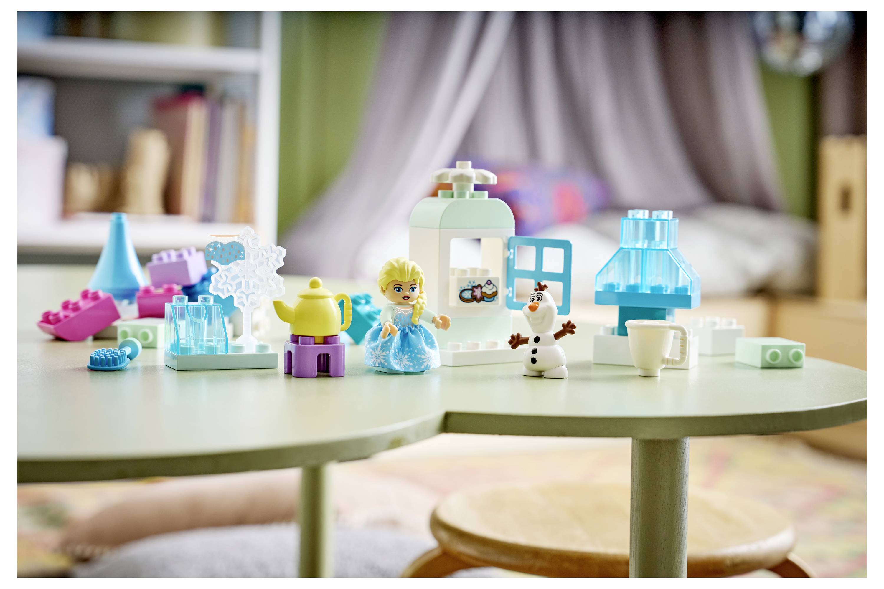 Spielbausteine und kleine Figuren, die auf einem Spieltisch in einem Kinderzimmer angeordnet sind, mit einem Miniaturhaus und Möbelstücken.