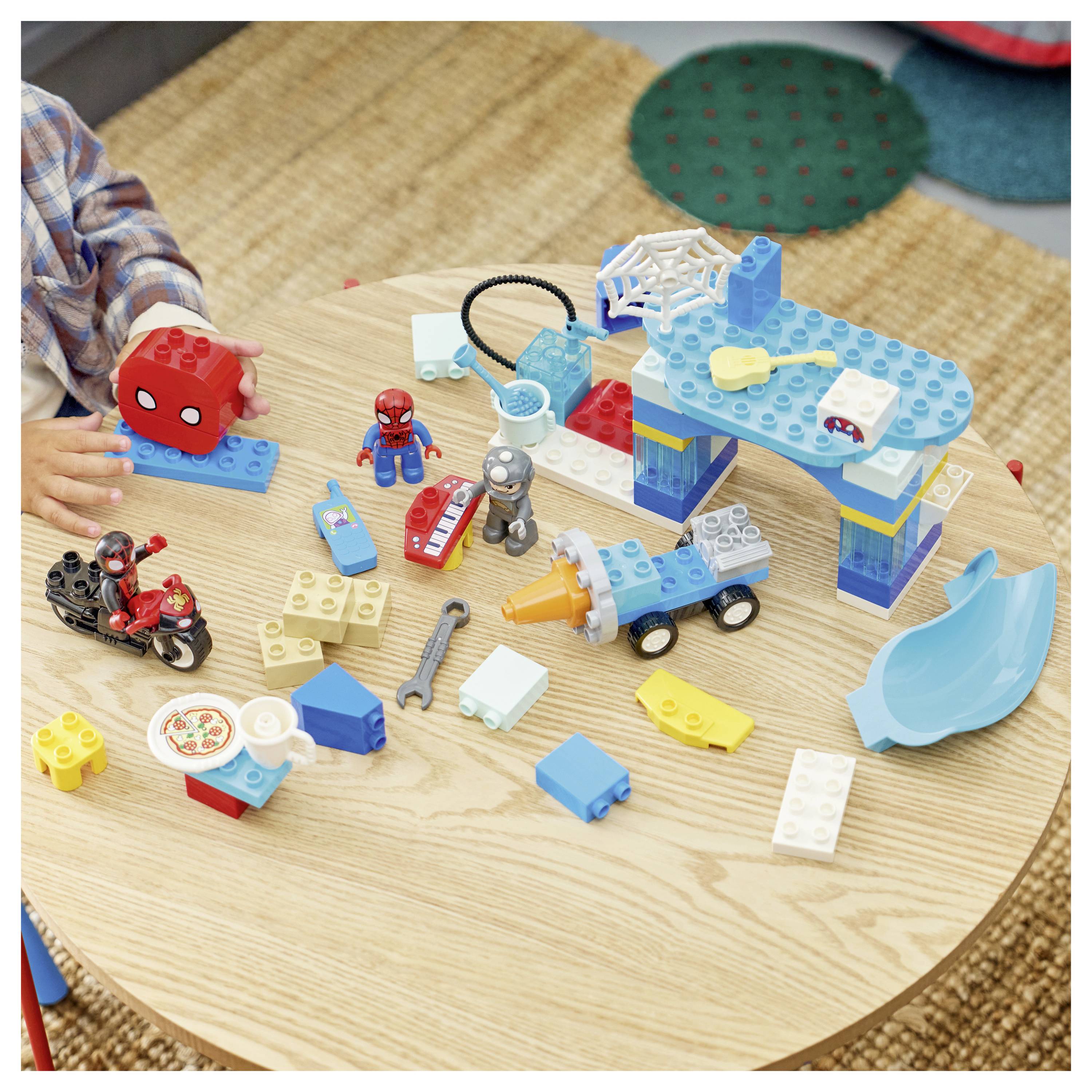 Kinderspieltisch mit assortierter LEGO-ähnlicher Bauteile, einschließlich Spider-Man-Figuren, Fahrzeuge, eine Brücke, Rutsche und verstreute Blöcke.
