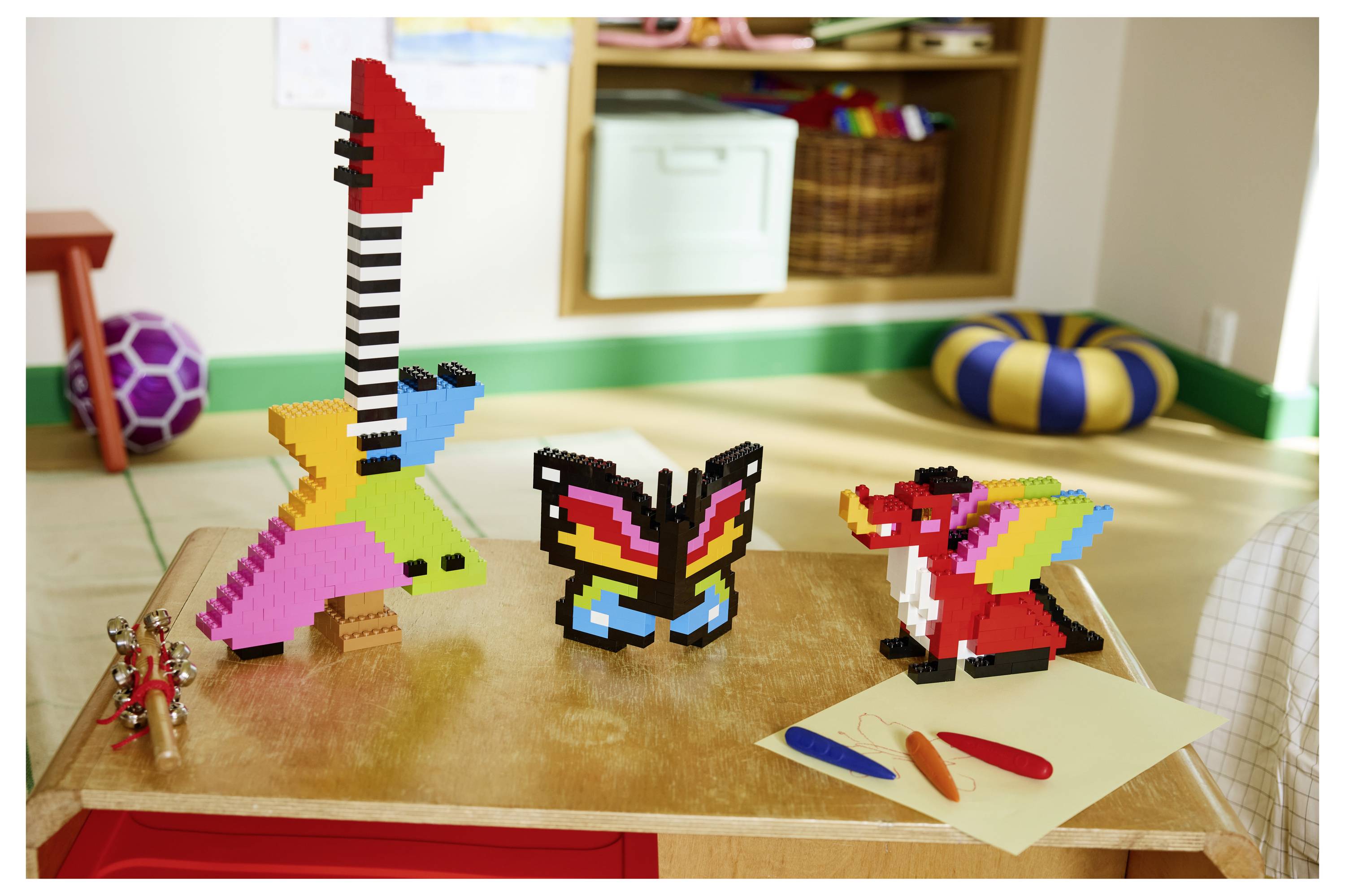 Eine Tischplatte mit einer Anzeige aus bunten, aus Bausteinen zusammengesetzten Tierfiguren, darunter ein Schmetterling und ein Vogel, angeordnet in einem Kinderspielzimmer.
