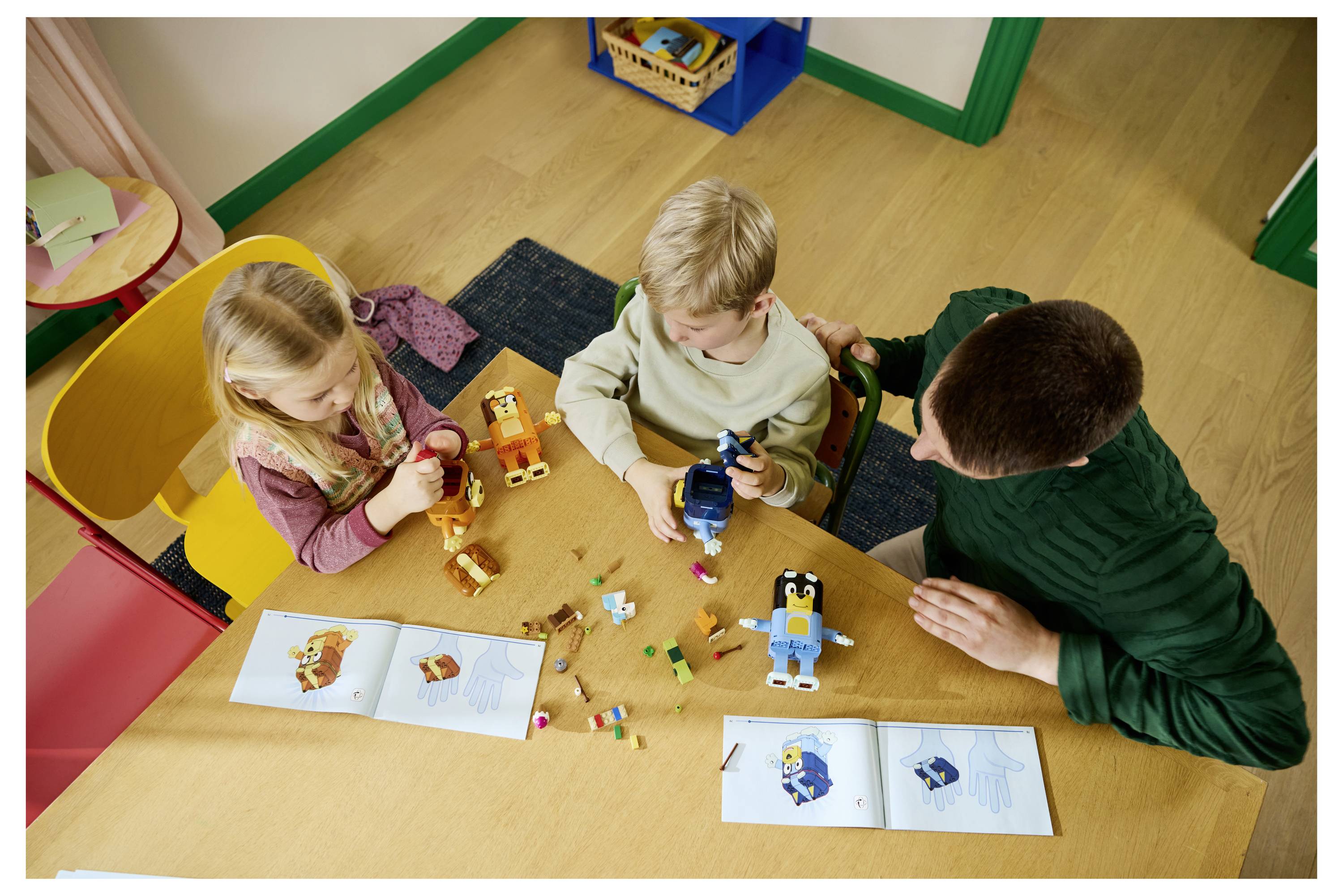 Drei Kinder sitzen um einen Tisch herum und bauen mit Spielzeugblöcken und Roboterfiguren in einem Klassenzimmer, mit geöffneten Anleitungsheften vor sich.