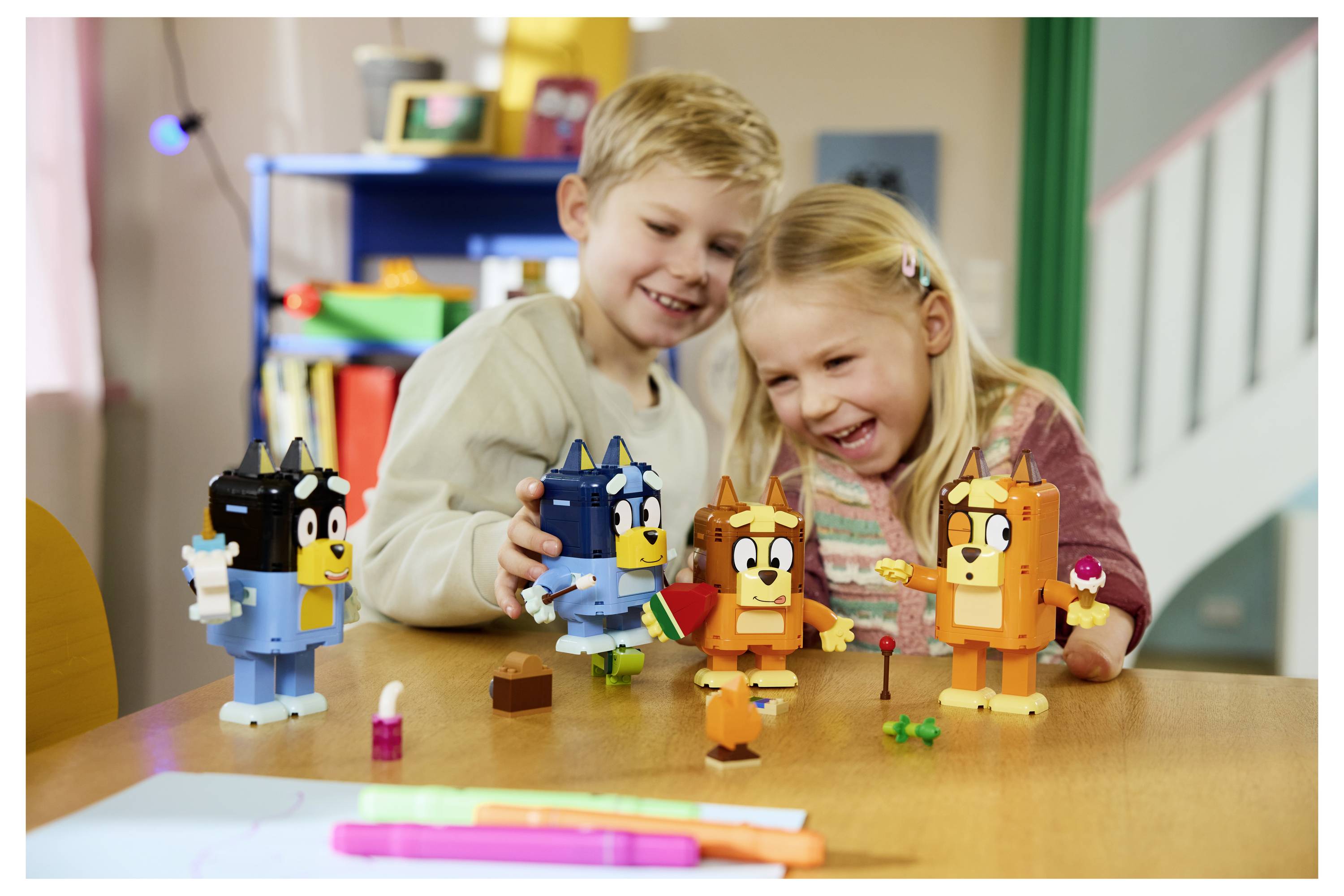 Zwei Kinder lächeln und spielen mit bunten Spielzeug-Tierfiguren an einem Tisch in einem Klassenzimmer oder Spielzimmer.