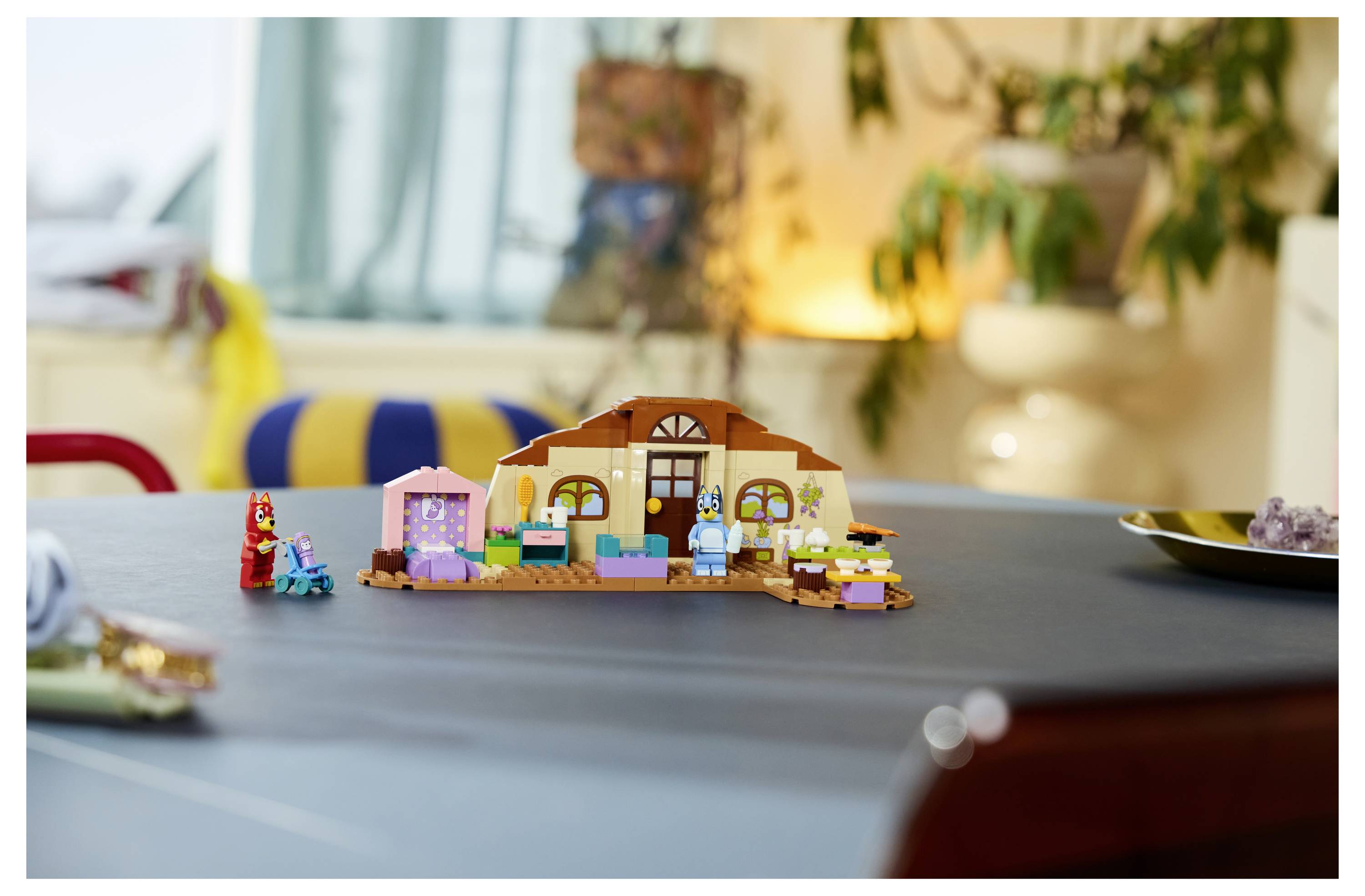 Eine kleine LEGO-ähnliche Hausszene auf einem Tisch, mit winzigen Figuren und Zubehör, in einer gemütlichen unscharfen Wohnzimmerumgebung.