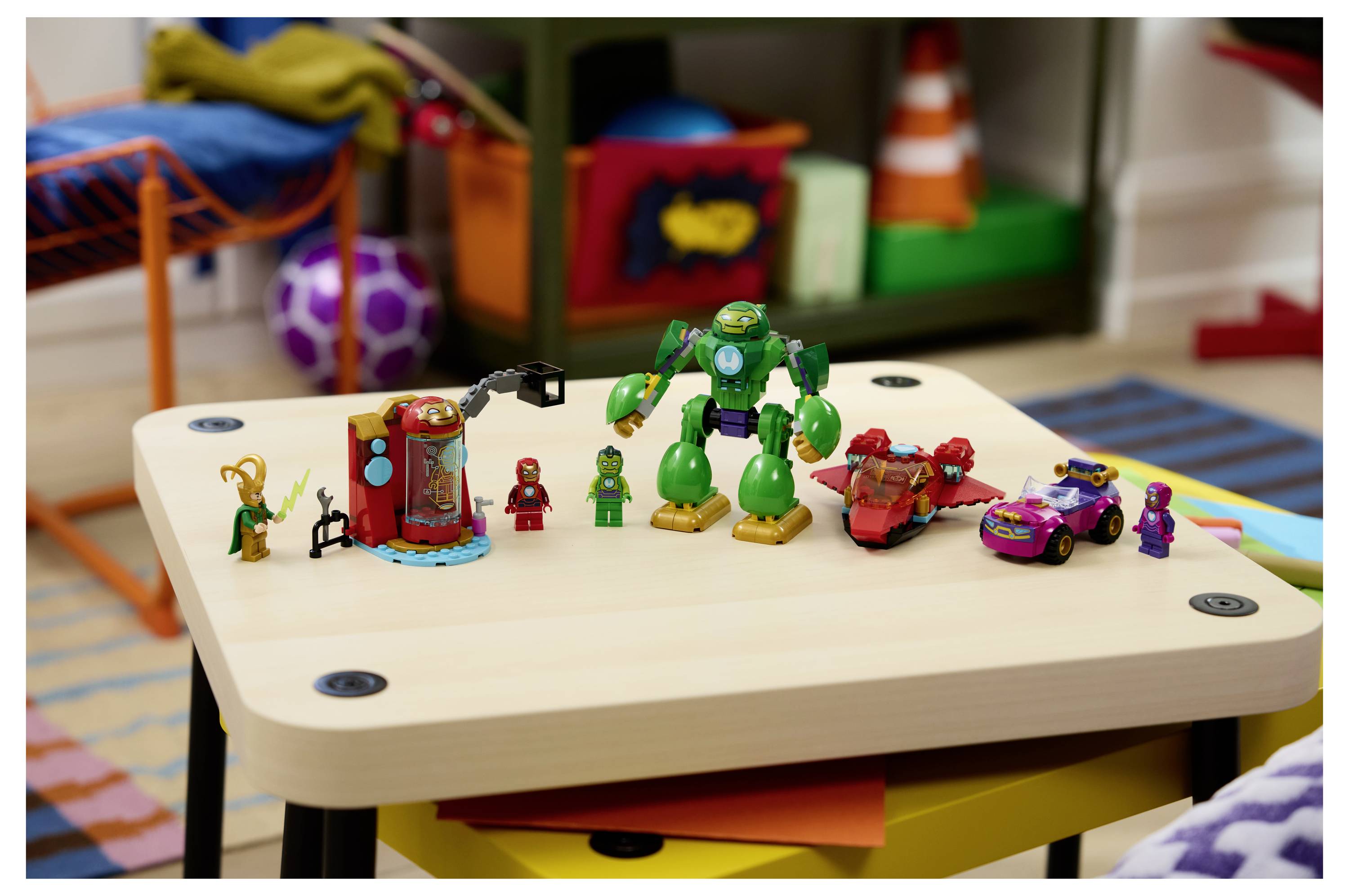 Spielzeug auf einem niedrigen Tisch angeordnet, einschließlich einer großen grünen Roboterfigur, einem roten Fahrzeug und kleinen Minifiguren in einem farbenfrohen Spielzimmer.