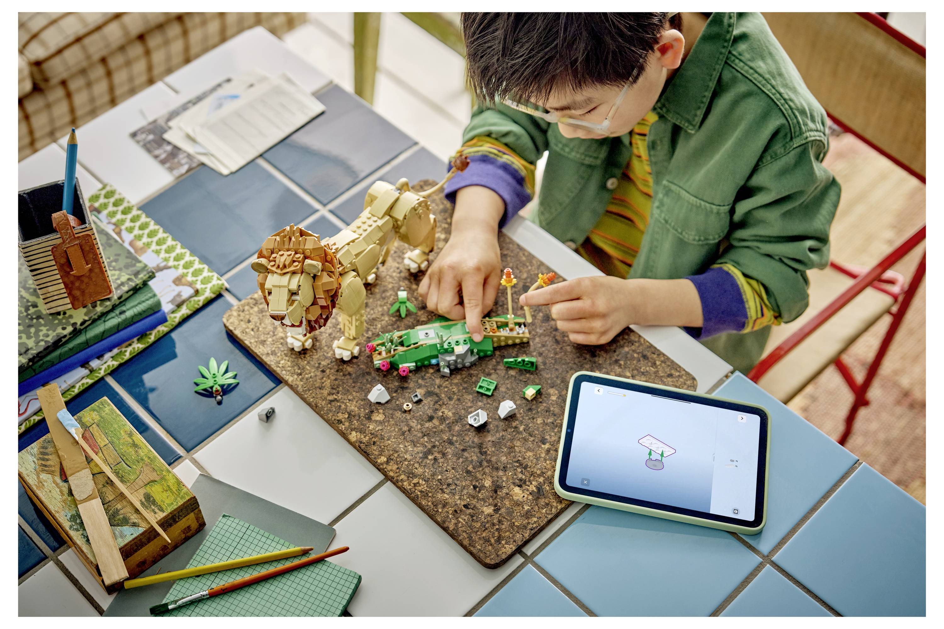 Ein Kind, das eine Maske trägt, baut eine kleine Block- und Roboter-Szene auf einem Tisch, während ein Tablet in der Nähe die Designanweisungen anzeigt.