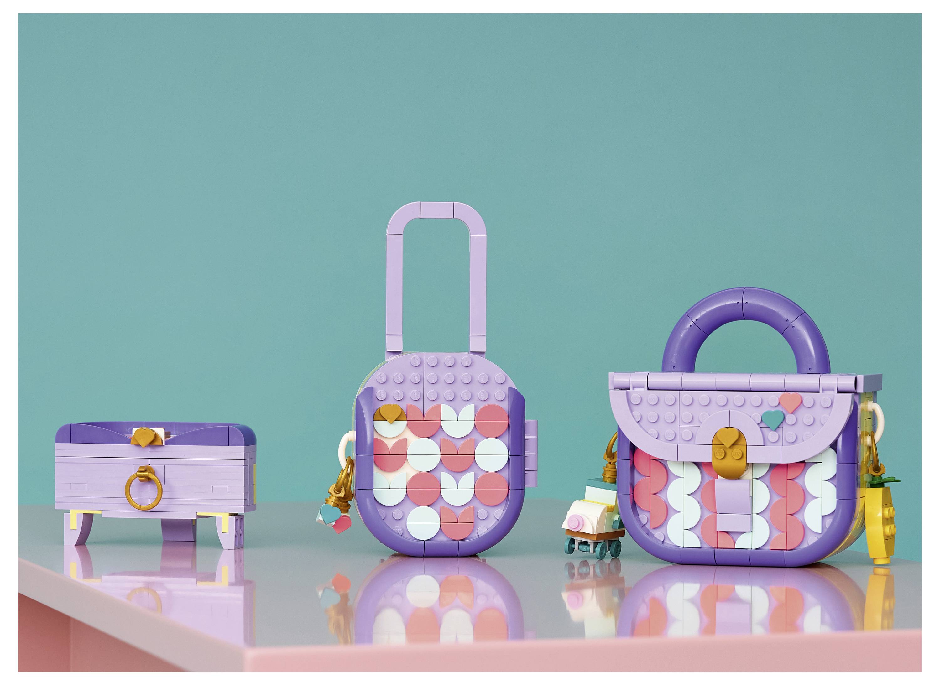 Drei pastellviolette Spielzeugtaschen aus Bausteinen werden auf einer reflektierenden Oberfläche vor einem blaugrünen Hintergrund präsentiert.