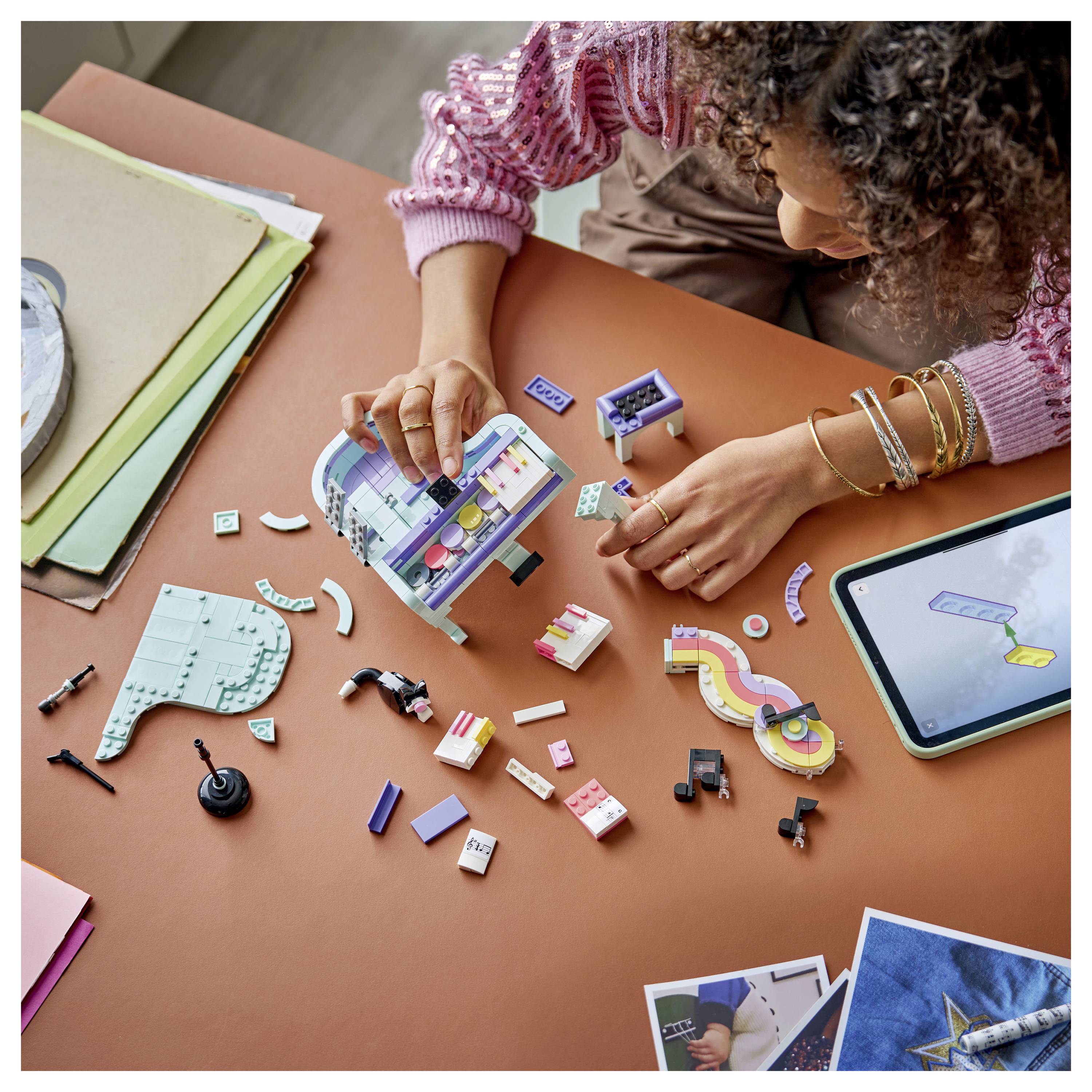 Eine Person baut ein buntes Miniatur-LEGO-ähnliches Bauprojekt an einem Tisch zusammen, mit losen Teilen, Anleitung und einem Tablet in der Nähe.