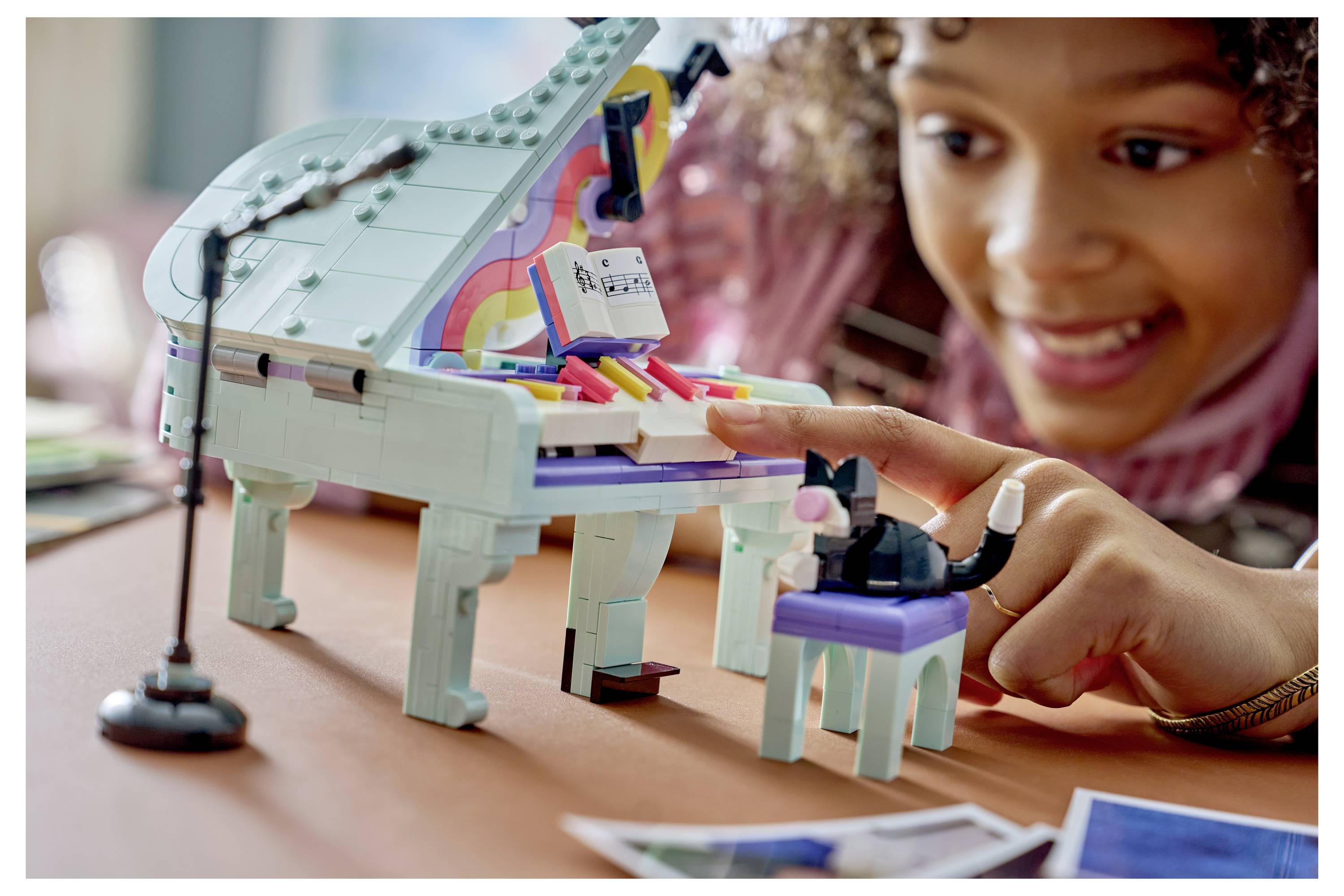 Ein Kind spielt mit einem LEGO-ähnlichen Spielzeugklavier-Set, drückt auf die Tasten und lächelt dabei das Modell auf dem Tisch an.