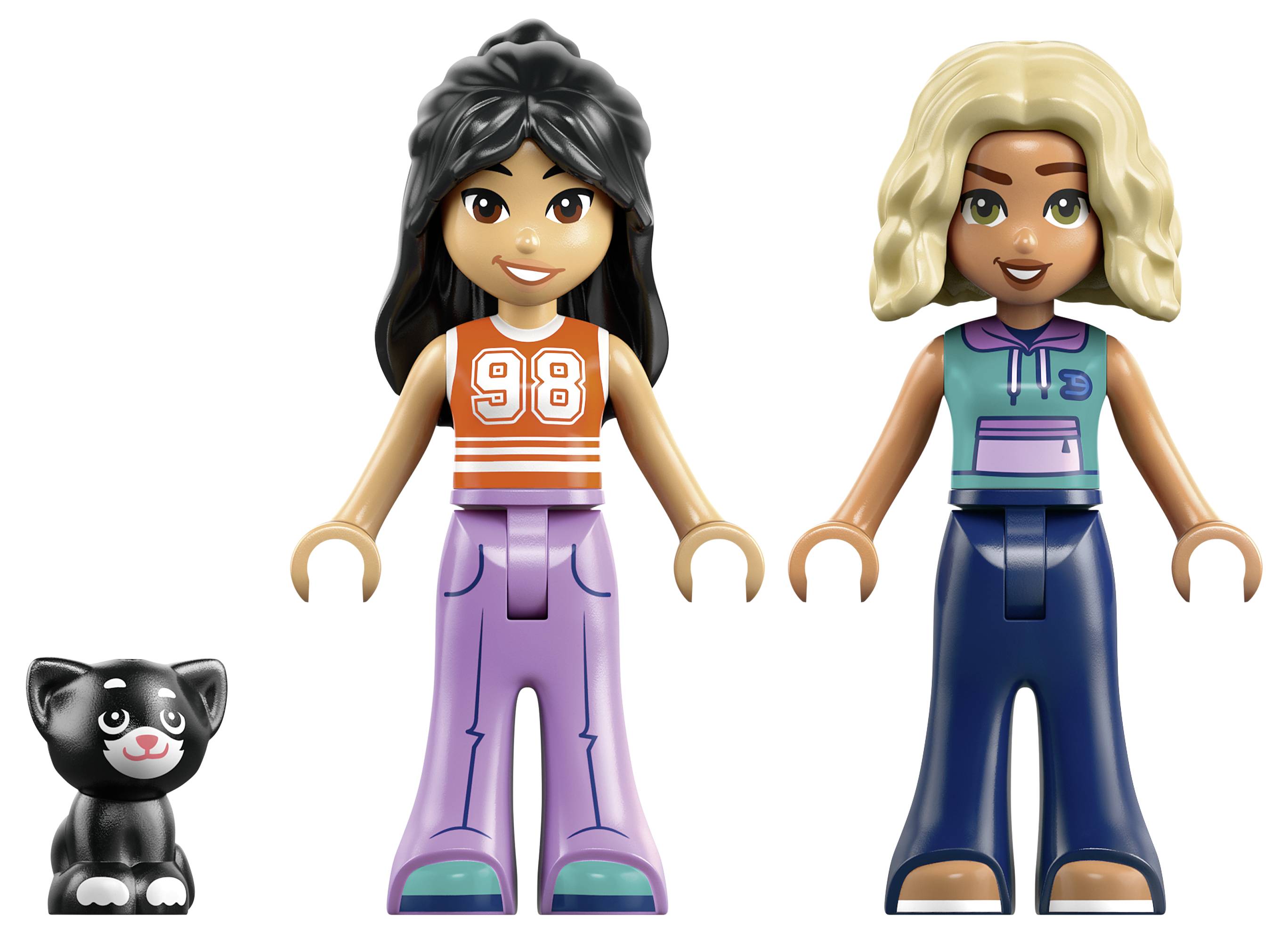 Zwei lächelnde Spielzeugfiguren, eine in einem orangefarbenen '98'-Oberteil und lila Hosen und eine in einem blaugrünen Oberteil und blauen Hosen, mit einer kleinen schwarzen Katzenfigur neben ihnen.
