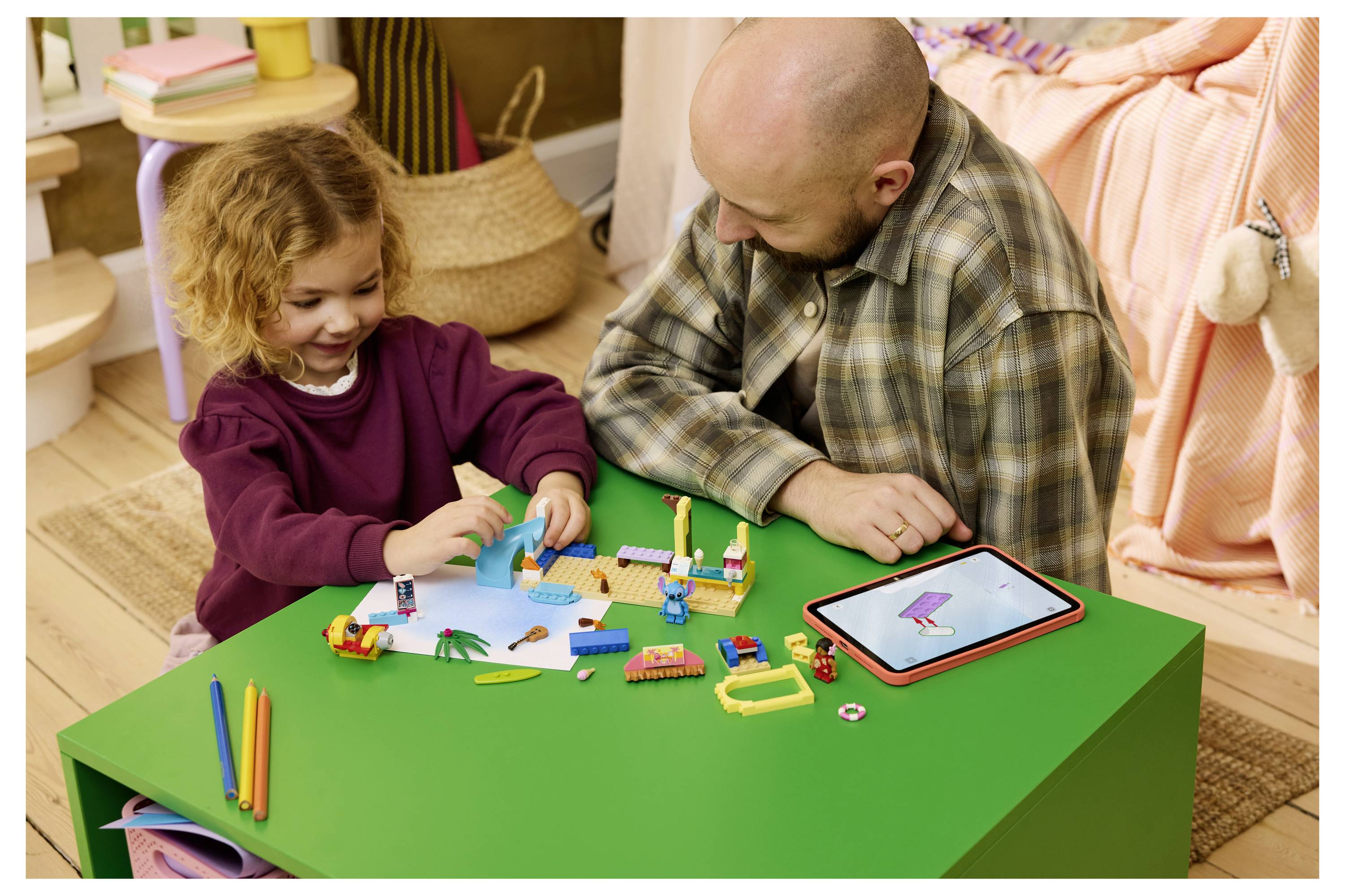 Erwachsener und junges Mädchen bauen mit bunten Spielziegeln an einem grünen Tisch, neben ihnen liegt ein Tablet, das eine Zeichen-App zeigt, in einem gemütlichen Zimmer.