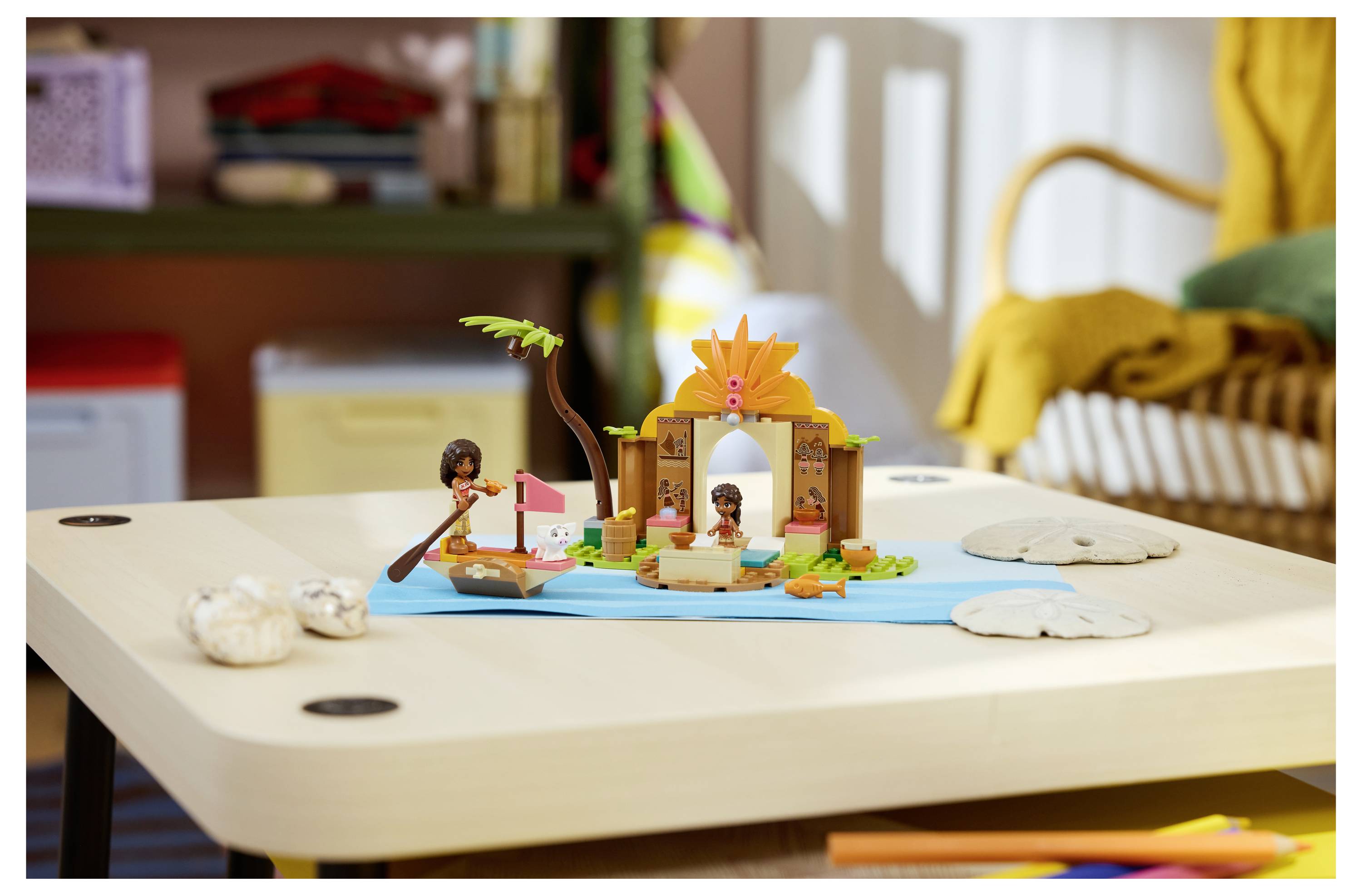 Miniatur-Strandszene eines Kindes mit Spielfiguren, einem Boot, einer Palme und einer kleinen Hütte auf einem Tisch.