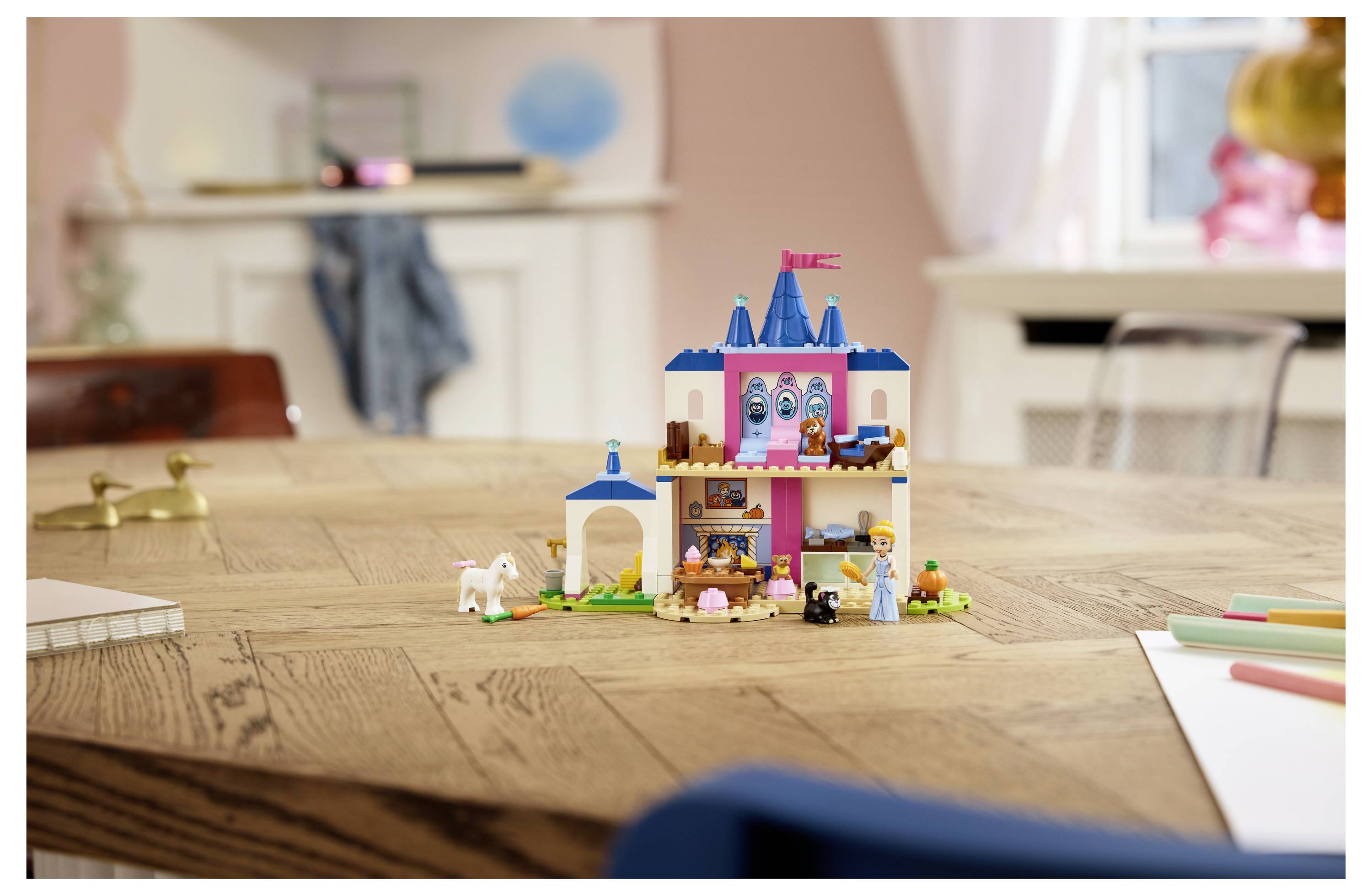Ein farbenfrohes Spielzeugschloss-Set mit kleinen Figuren und Tieren steht auf einem Holztisch in einem hellen Raum.