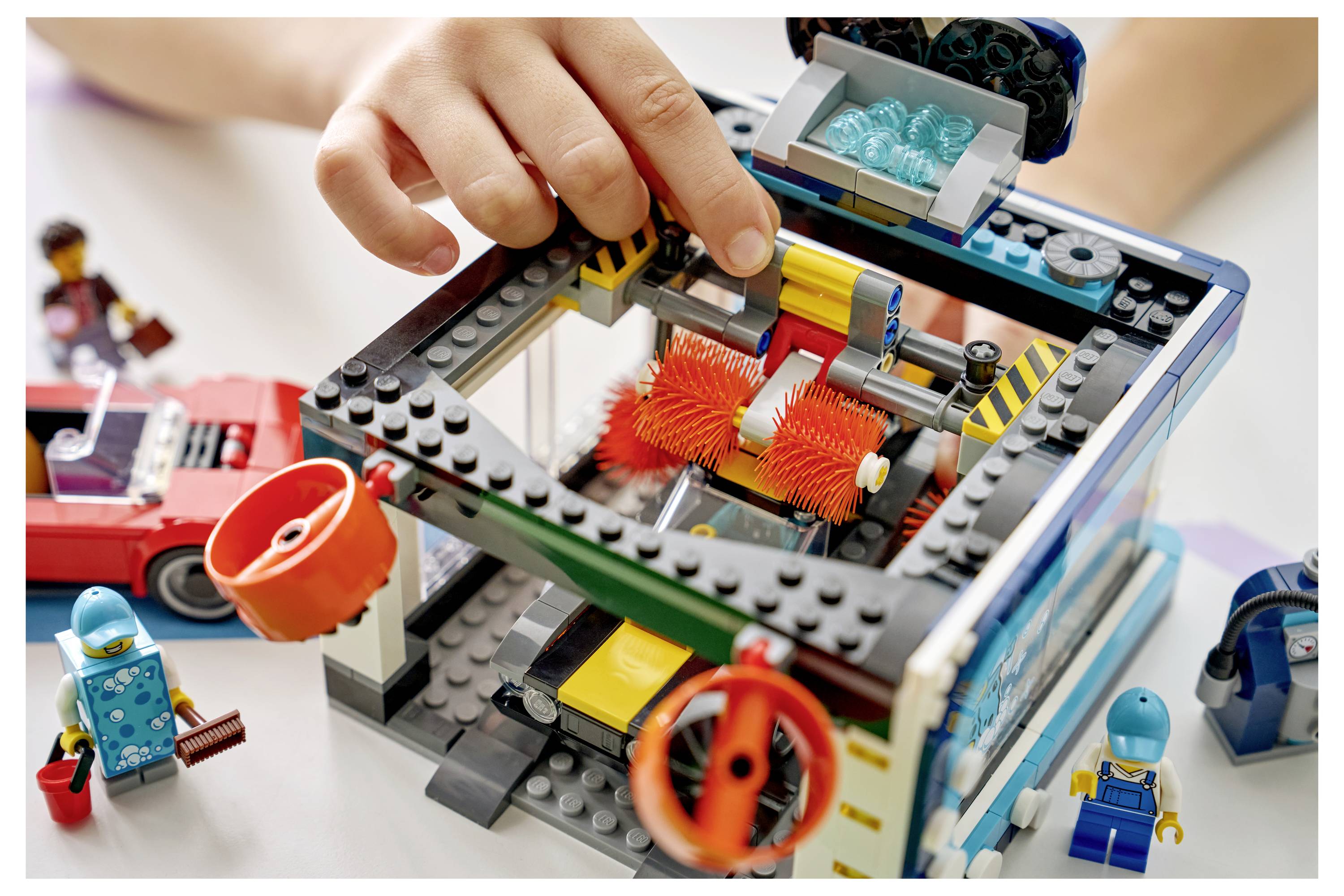 Kind spielt mit einem LEGO-ähnlichen Maschinenmodell, passt ein transparentes Dach über orangefarbenen rotierenden Zahnrädern an, mit kleinen Minifiguren in der Nähe.