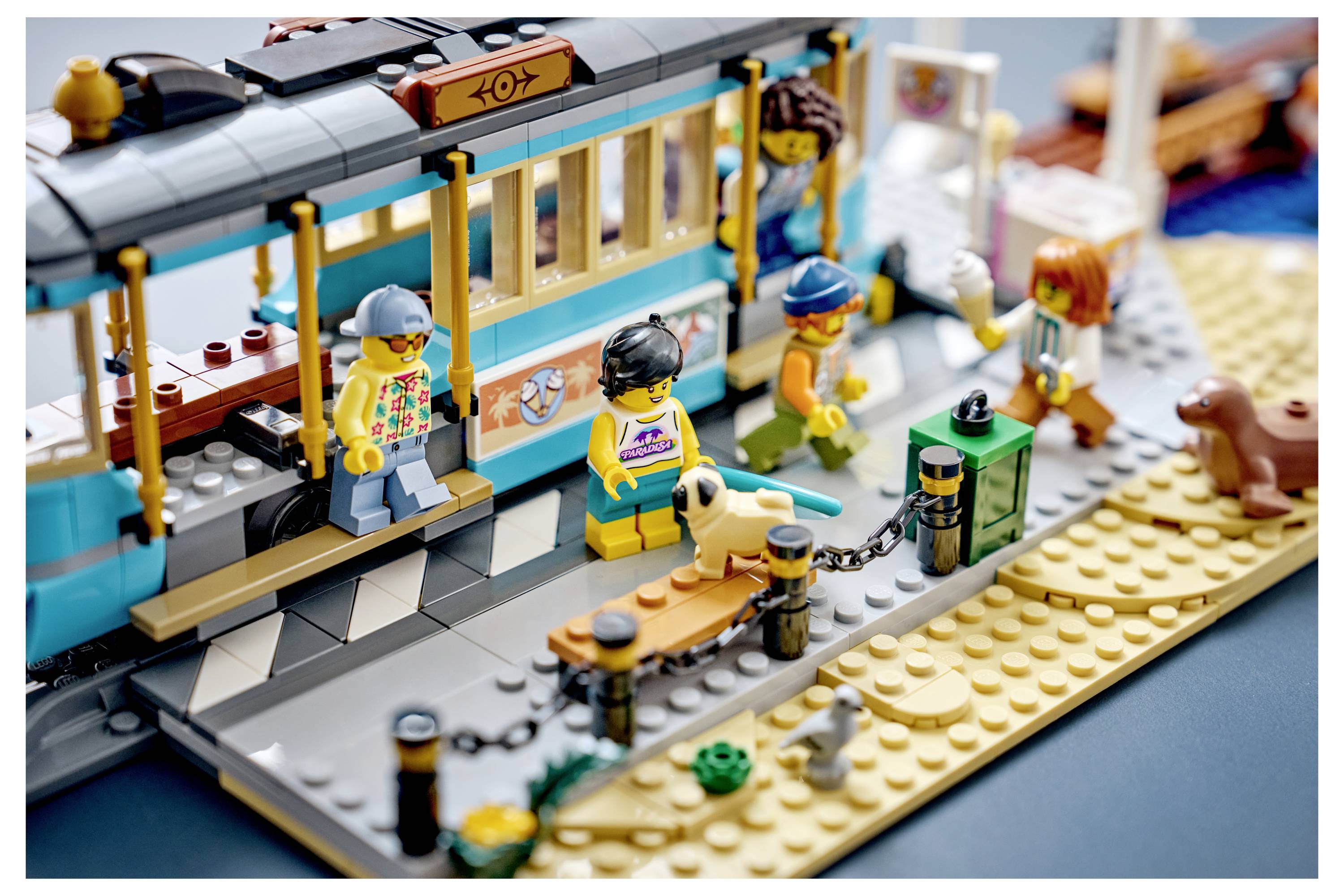 LEGO-Strandbahnszene mit Fahrgästen beim Einsteigen, einschließlich eines Hundes im Sand in der Nähe der Haltestelle.