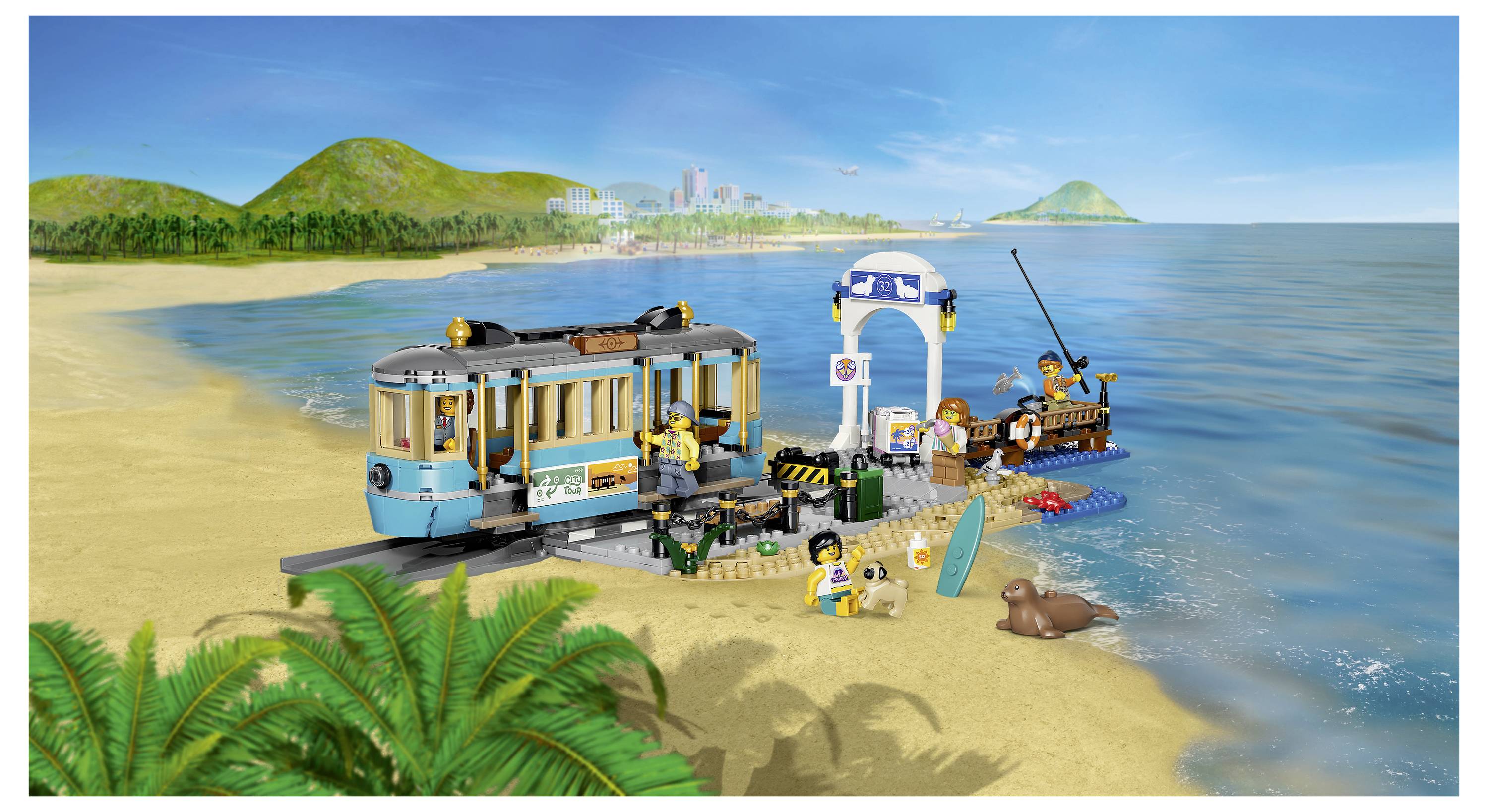 Spielzeug-Strandszene mit einer blauen Straßenbahn, Rettungstower, kleinem Boot, Minifiguren und Meerestieren neben ruhigem Wasser und entfernten Hügeln