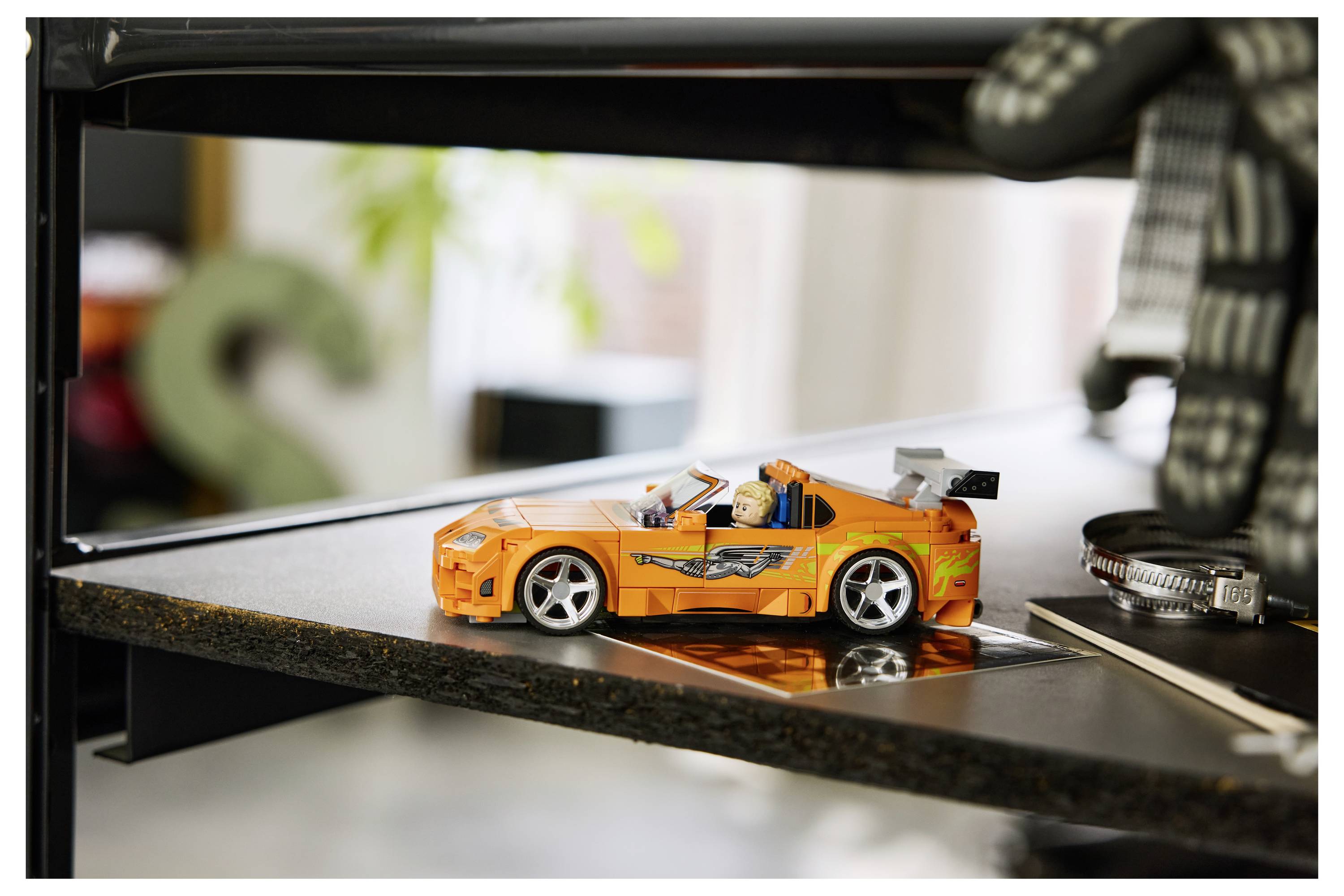 Oranges Spielzeug-Sportauto auf einer reflektierenden 3D-Drucker-Bauplattform, mit dem sichtbaren Drucker-Rahmen drumherum.