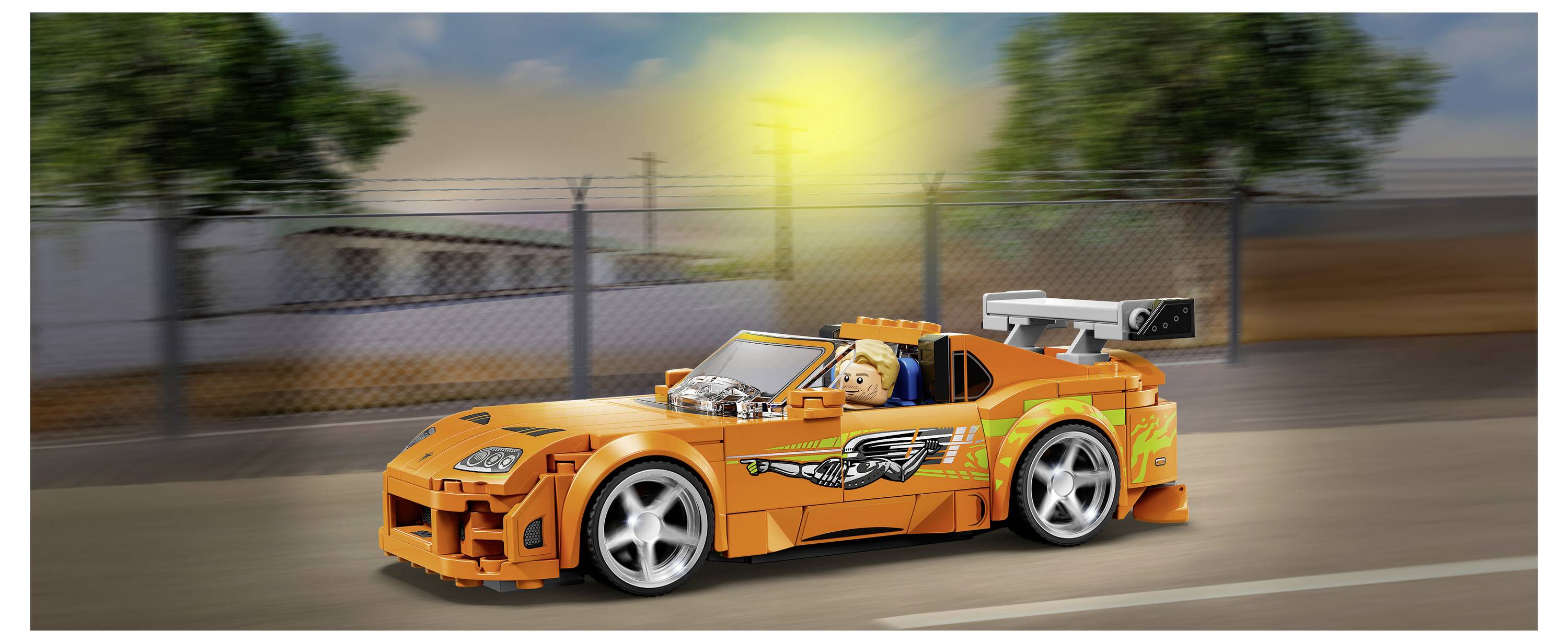 Orangenes Spielzeugrennauto, das auf einer Straße fährt, mit einem Hundefahrer und einem großen Heckflügel.