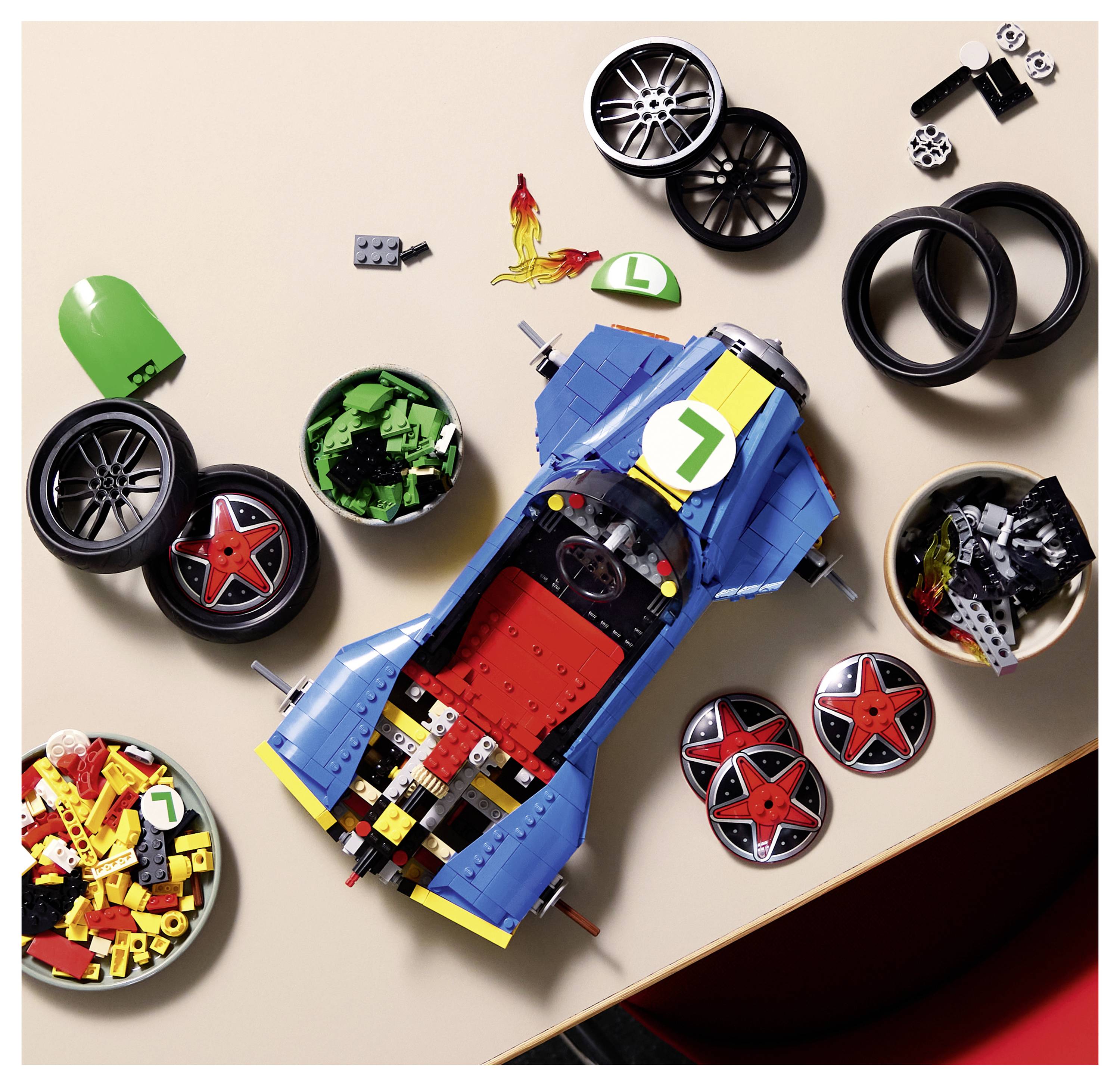 Draufsicht auf ein blaues LEGO-Rennwagen-Modell, umgeben von lockeren Rädern, Reifen und Teilen auf einer Tischplatte.