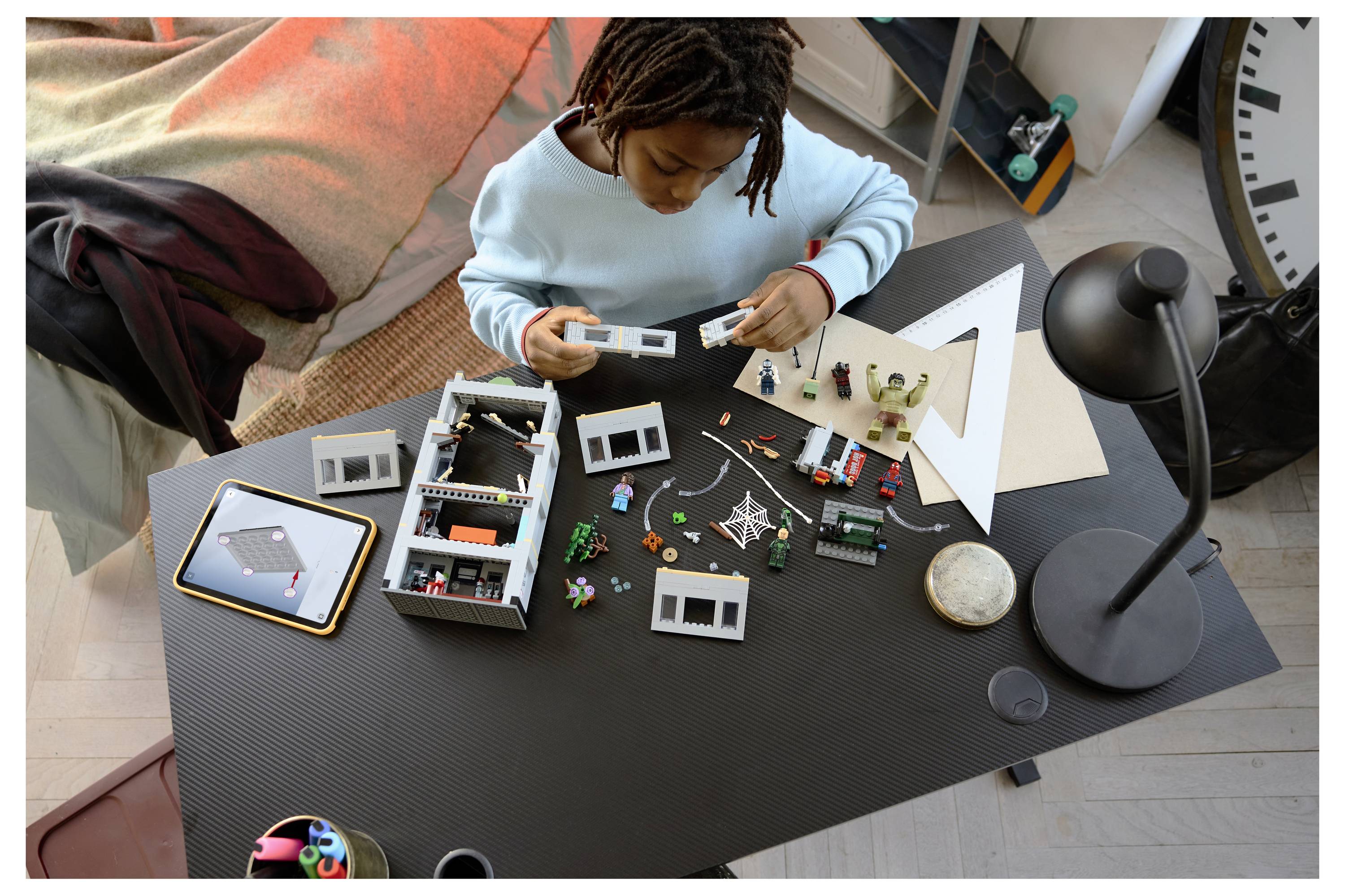 Ein Kind montiert ein LEGO-ähnliches Modell auf einem schwarzen Tisch, mit verstreuten Teilen, kleinen Figuren und einer Schreibtischlampe in der Nähe.