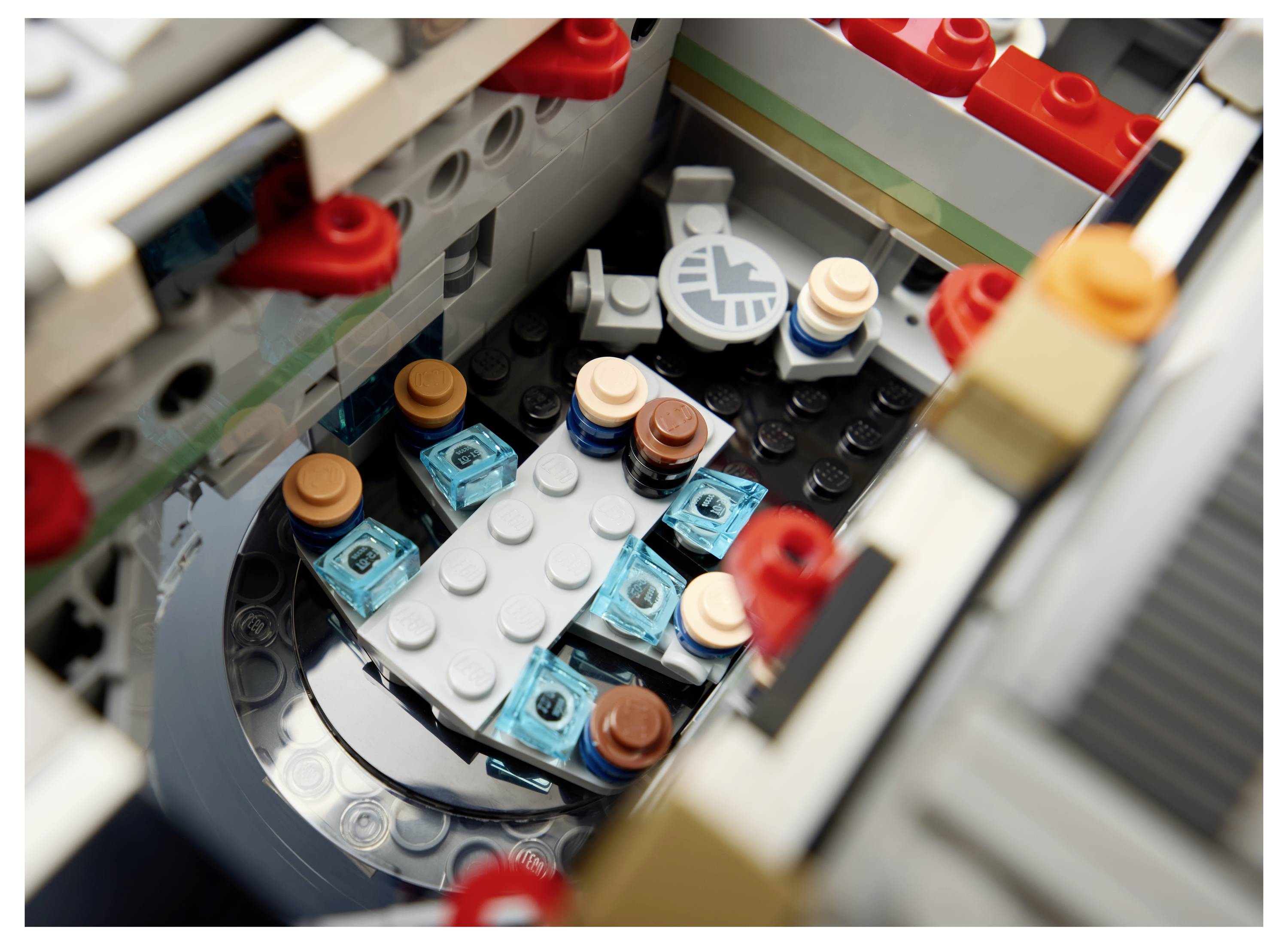 Nahaufnahme eines LEGO-Bauerinterieurs mit einem kleinen runden Tisch und vier Minifiguren-Sitzen in einem grauen Raum.