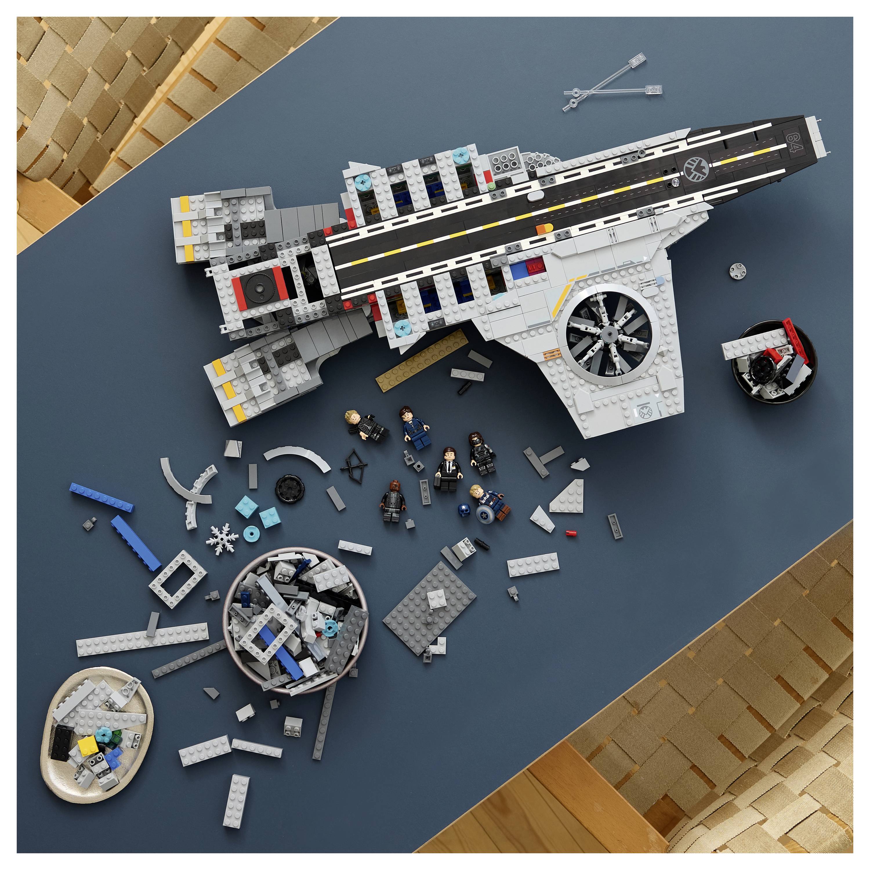Aufsicht auf ein zusammengebautes LEGO-Raumschiffmodell mit verstreuten Teilen und Minifiguren auf einem blauen Tisch.