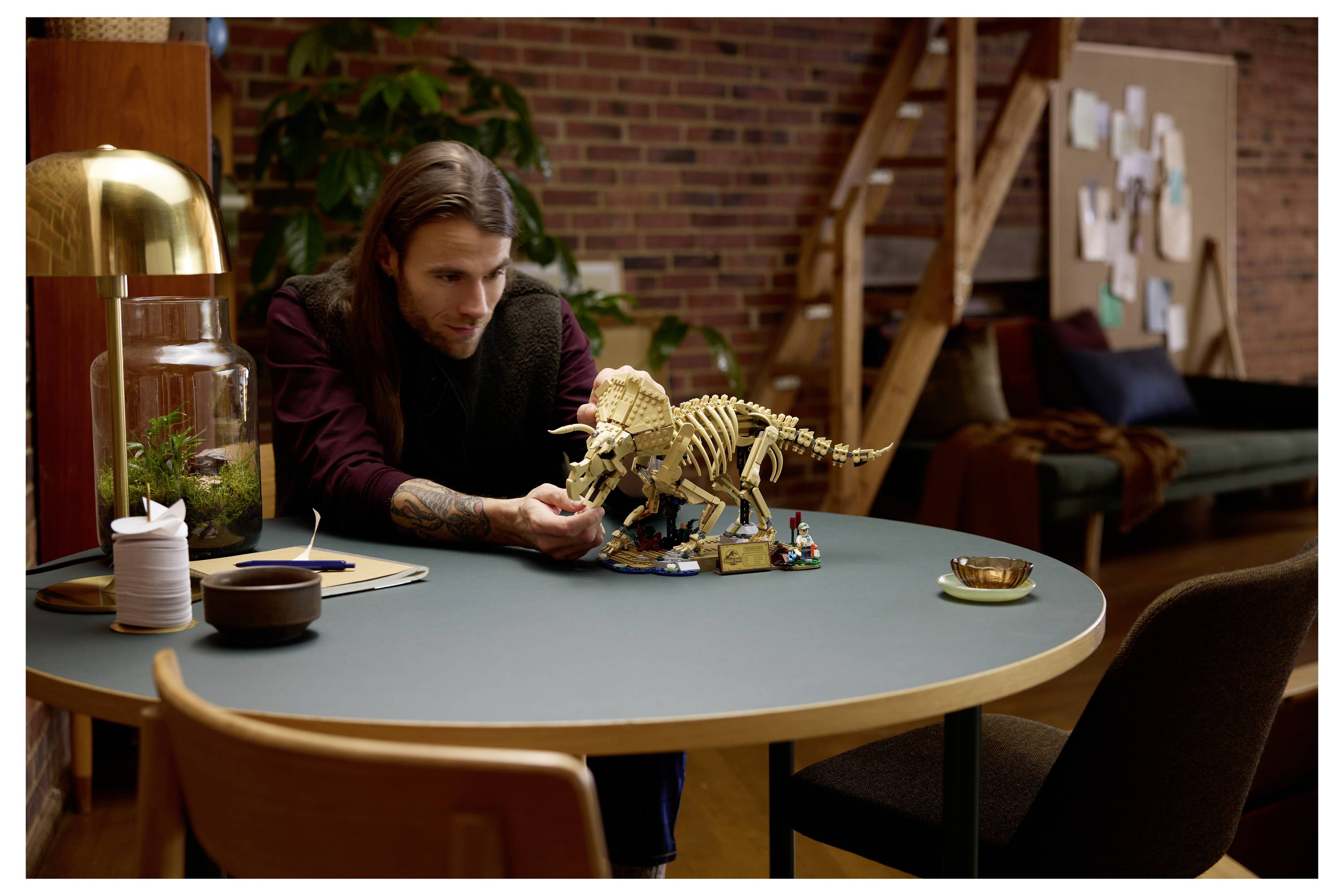 Ein Mann studiert ein Dinosaurier-Skelett-Modell auf einem runden Tisch in einem gemütlichen Studio, mit anderen LEGO-Steinen in der Nähe.