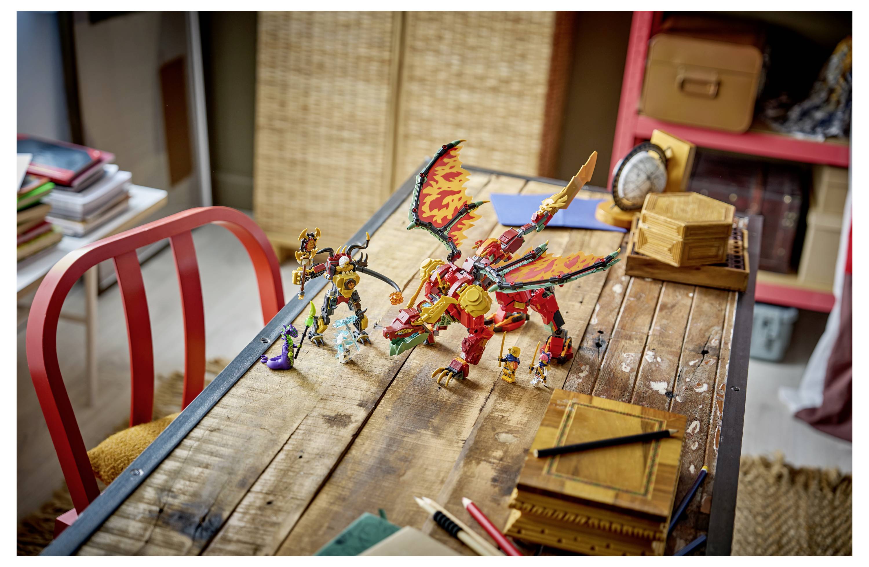 Zwei Spielzeugdrachenfiguren und eine kleine Rüstungsfigur sind auf einem Holztisch in einem Kinderspielzimmer oder Bastelbereich angeordnet.