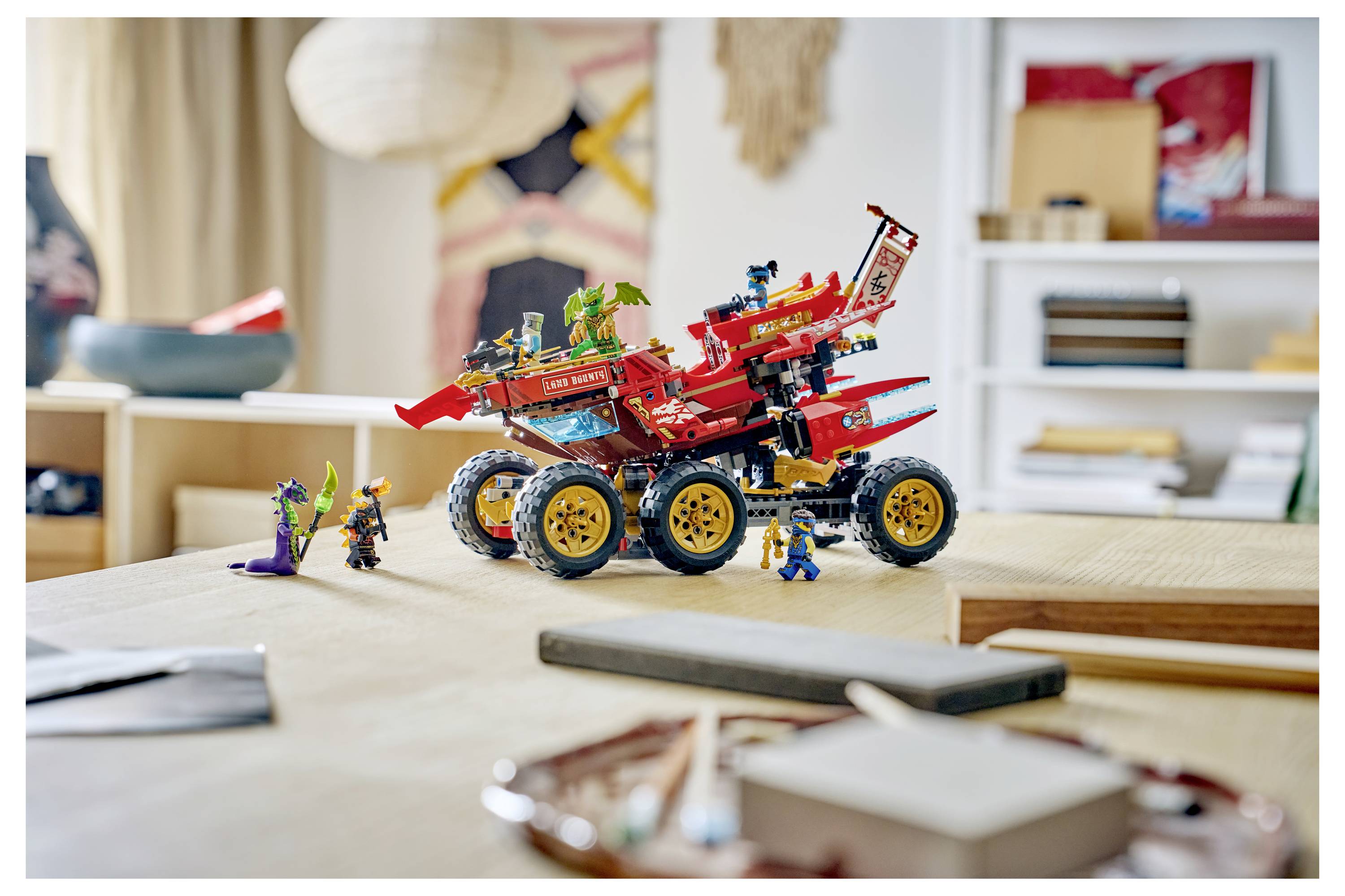 Ein rotes LEGO-ähnliches Geländefahrzeug mit Minifiguren sitzt auf einem Tisch in einem Wohnzimmer, dargestellt in einer Nahaufnahme einer Innenszene.