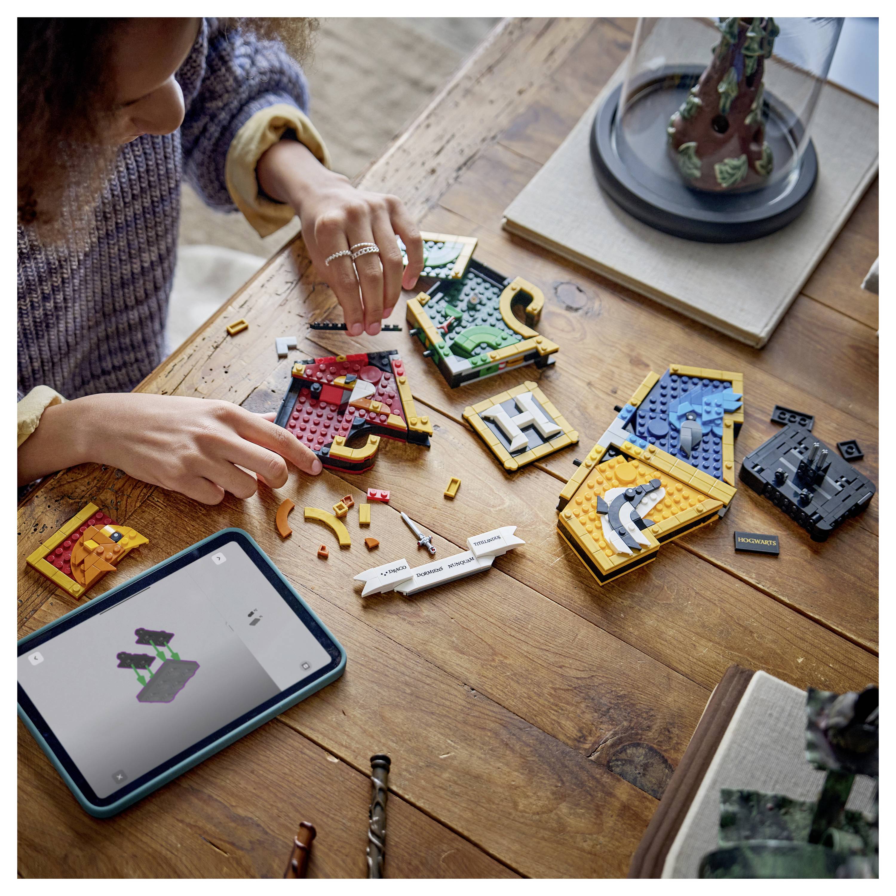 Eine Person, die LEGO-ähnliche Buchstabenkacheln auf einem Holztisch zusammensetzt, mit einem Tablet, das die Bauanleitung zeigt.